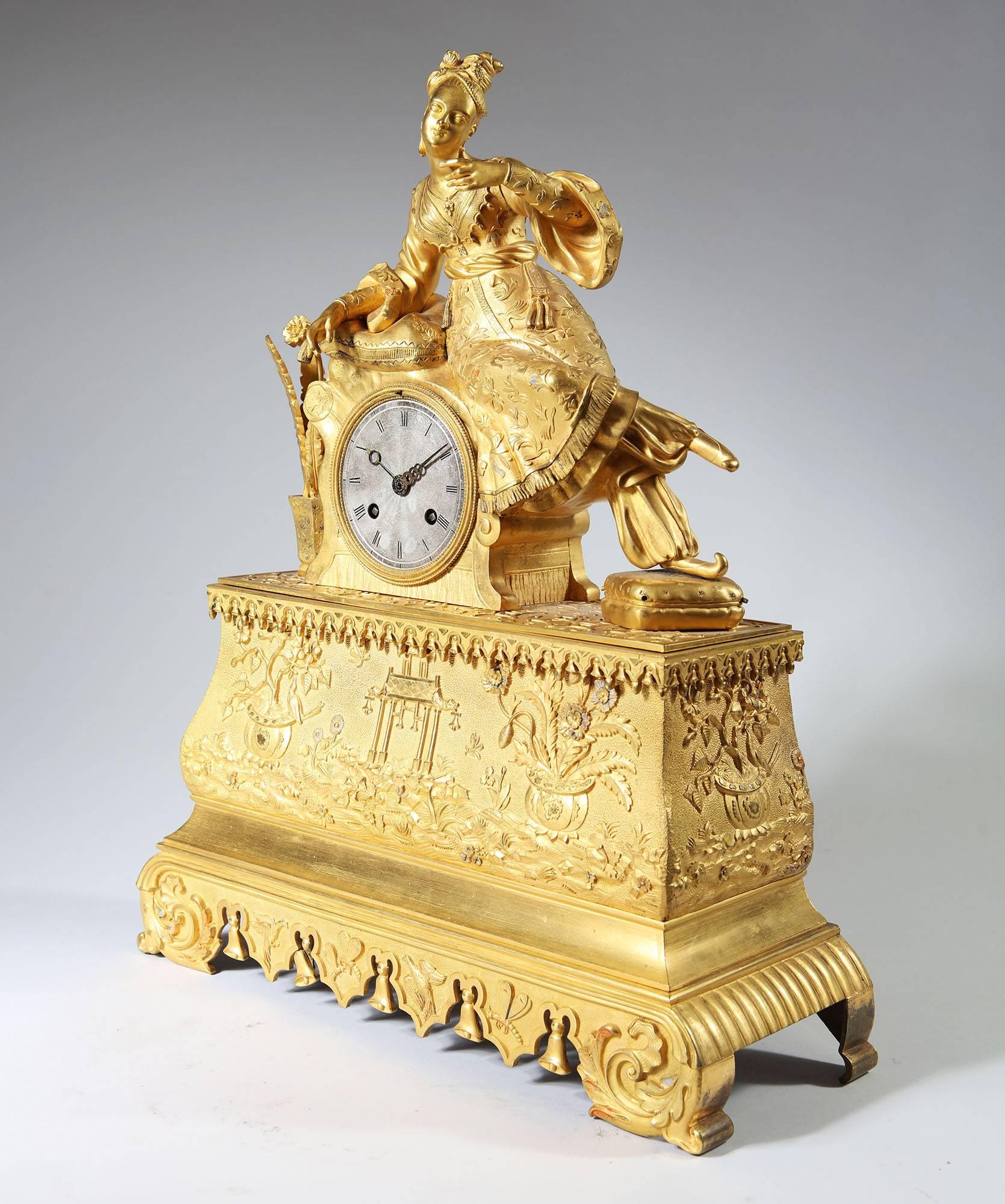 Pendule en bronze doré du XIXe siècle représentant une dame assise en robe ottomane reposant sur des coussins, le bras levé tenant peut-être à l'origine un oiseau ou un objet similaire. Surmontée d'une base ogivale avec un riche ornement de paniers