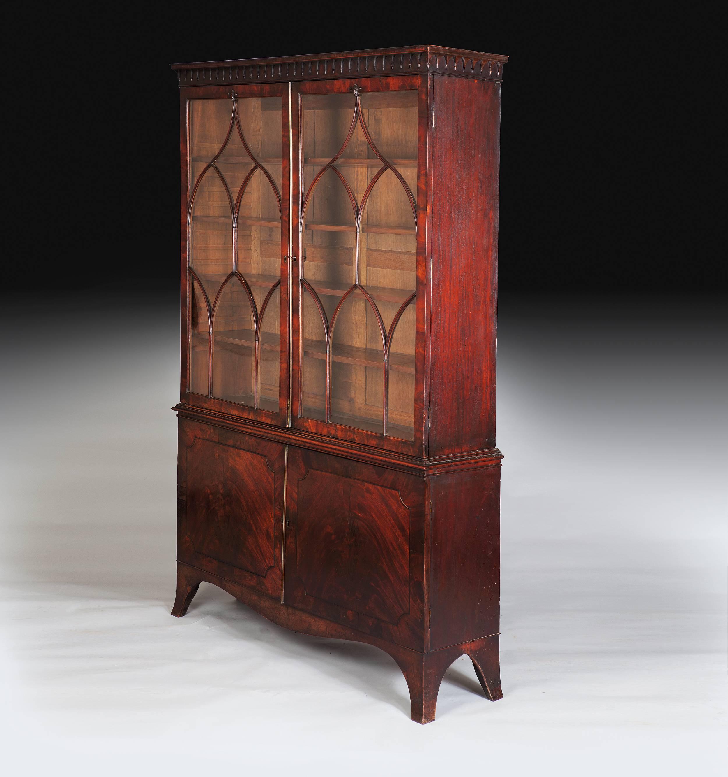 England, 1770.

A fine late 18th century George III mahogany bookcase, the upper section with glazed doors and Gothic mullions opening to a shelved interior below a fine frieze with Gothic pendants. Above cupboard doors with rich figuring opening