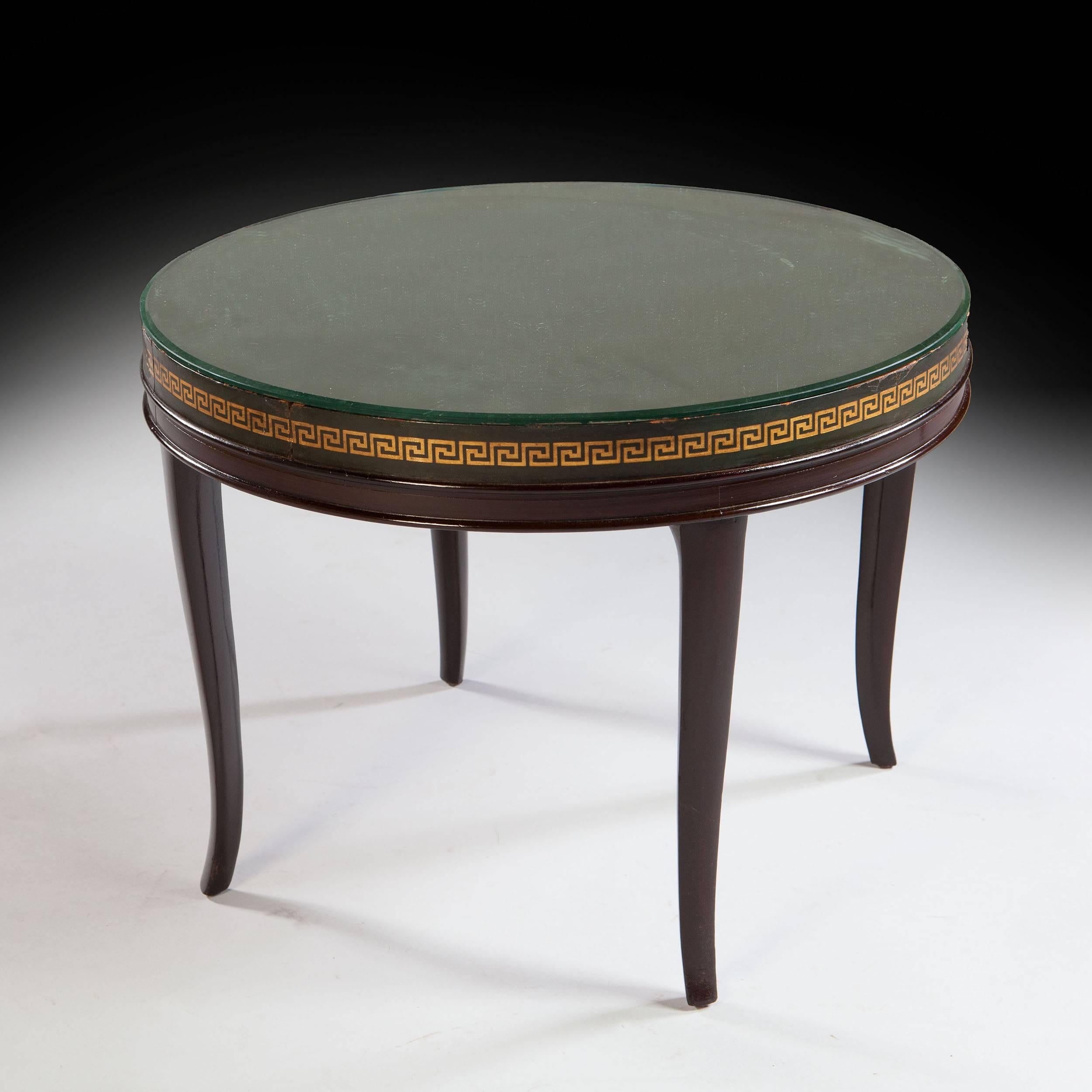 A mid-20th century Art Deco round occasional table, retaining its original beveled mirror top, above a leather frieze with Greek key gilt tooled ornament, the whole raised on curved tapering legs.

Stamped on the underside, Property of the Savoy