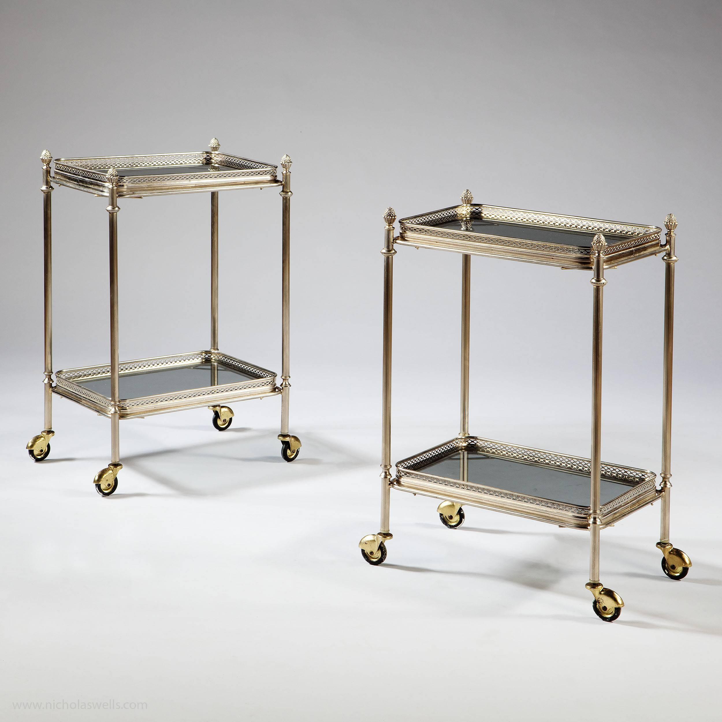 Fabulous pair of nickel-plated two-tier trolley tables, the reeded legs with cast finials and rubber wheels, each with two removable trays with pierced extruded borders and their original smokey glass inserts. 

Measures: Height 67cm 26.5in,