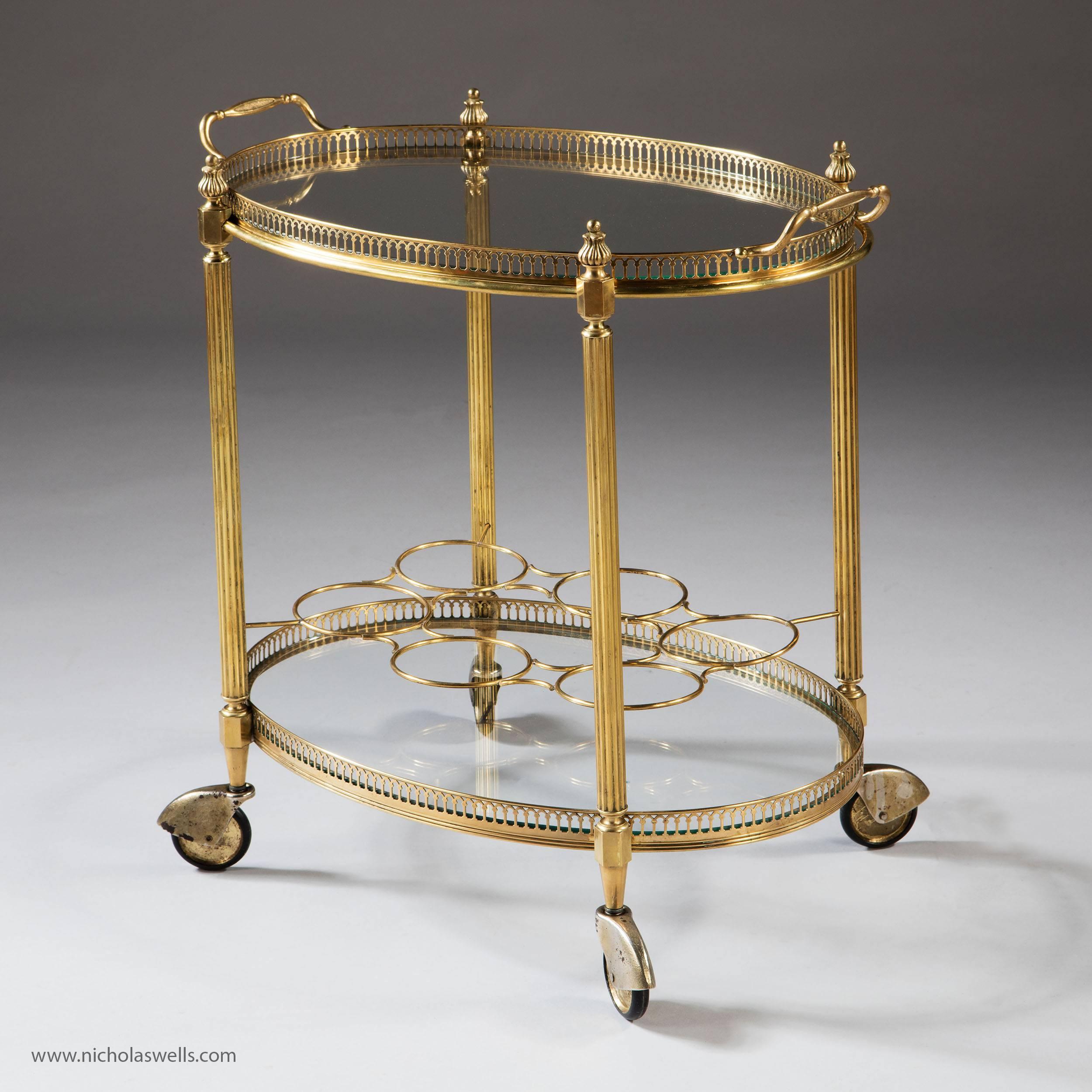 Fantastic Mid-Century French polished brass two tier drinks trolley of oval form, the upper removable tray above a six ring bottle holder, both with glass bottoms and pierced brass borders. Raised on brass and rubber castors. 

Measures: Height