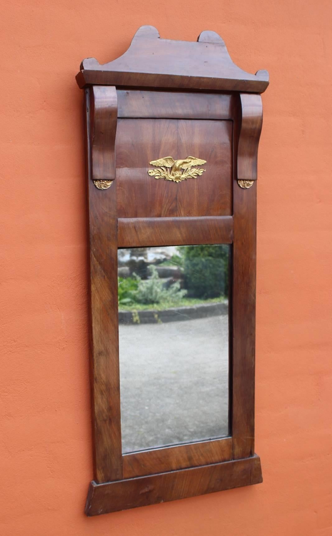 The Late Empire mahogany mirror, winged with elegant gold leaf, dates back to around 1840 and exudes a distinguished elegance and historical value. The mirror's sophisticated design and artistic details make it a remarkable piece of antique that