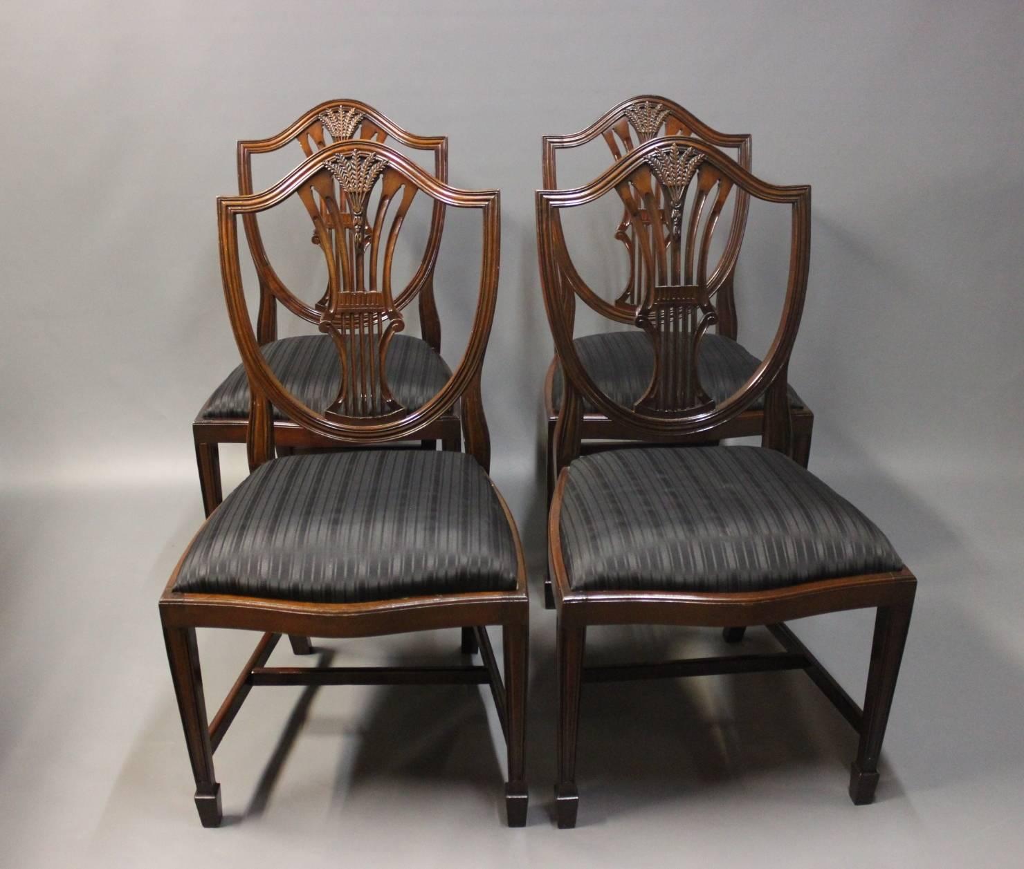 A set of four antique Hepplewhite dining room chairs by an unknown cabinetmaker from England and the 1920s. The chairs are in polished mahogany and upholstered in black fabric.