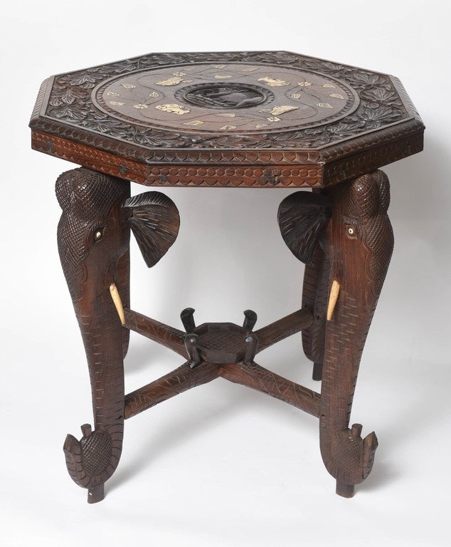 The deeply carved hardwood table is fashioned with 4 elephant heads  In addition, its top is inlaid with 