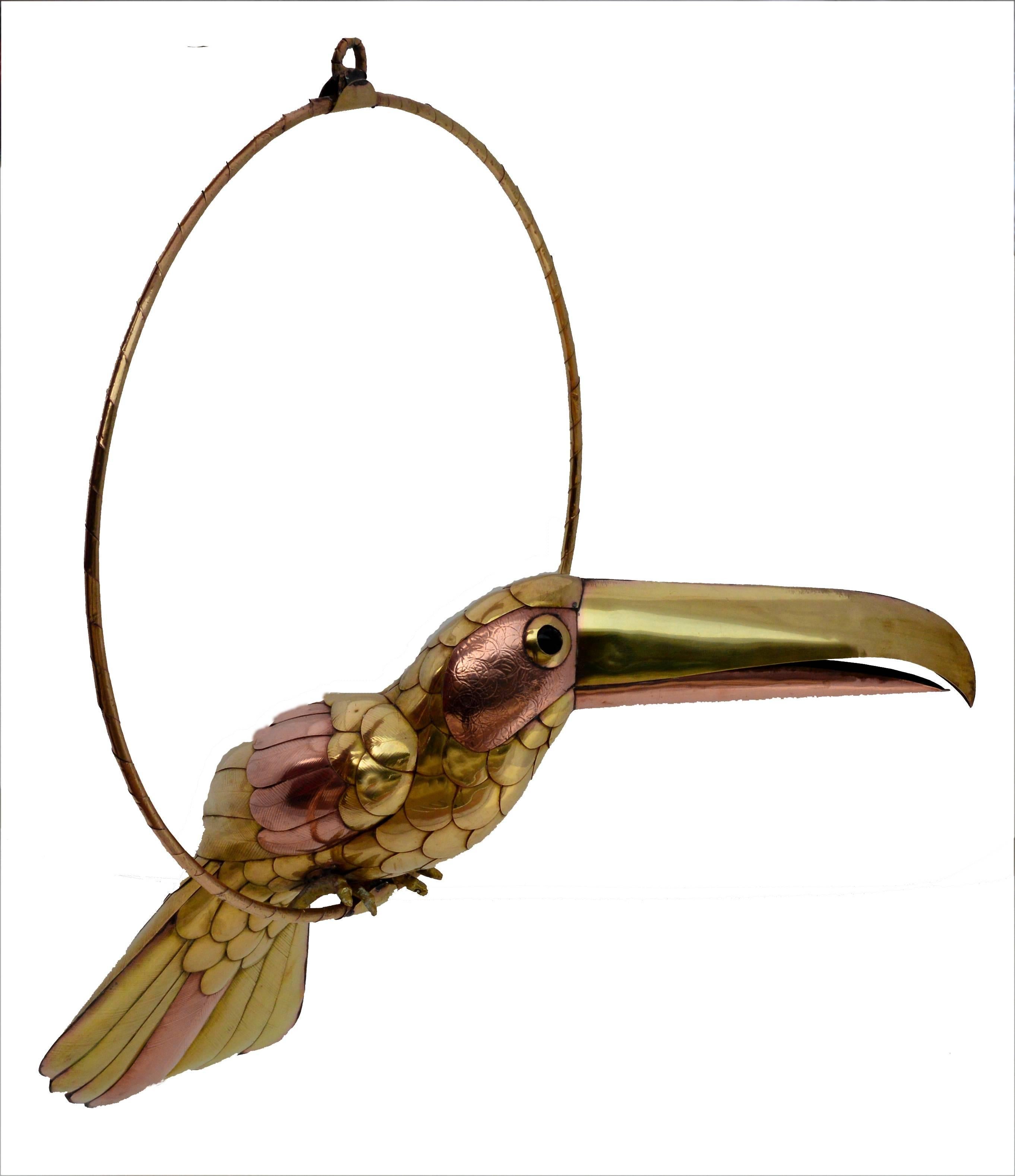 Whimsical brass and copper toucan sculpture by Mexican artist Sergio Bustamante (1934-2014). Toucan measures: 6" H x 16" L. Brass-wrapped hoop is 16" in diameter. 

Sergio Bustamante studied architecture at the University of