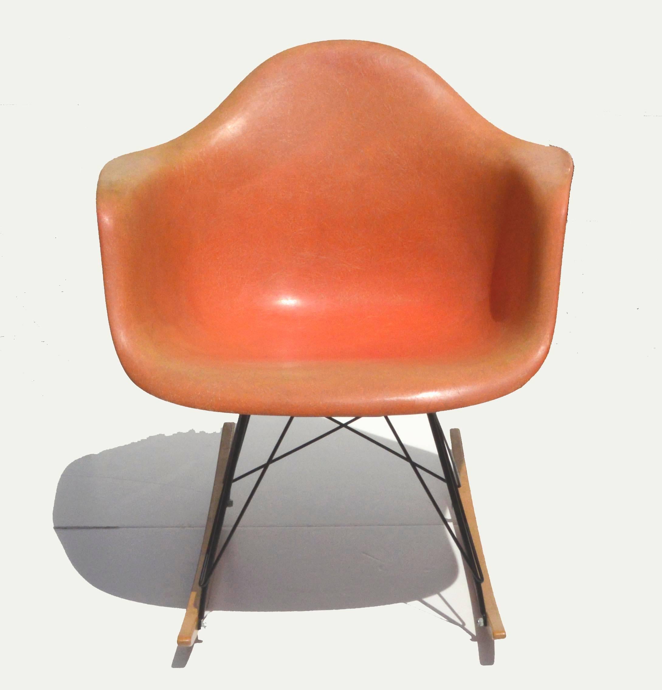 Gorgeous iconic salmon-orange fiberglass molded plastic rocking chair with black enamel base and birch rocking struts, circa 1960s. Second generation Charles and Ray Eames RAR rocker with the large shock mounts but no rope edge. Fading has given it