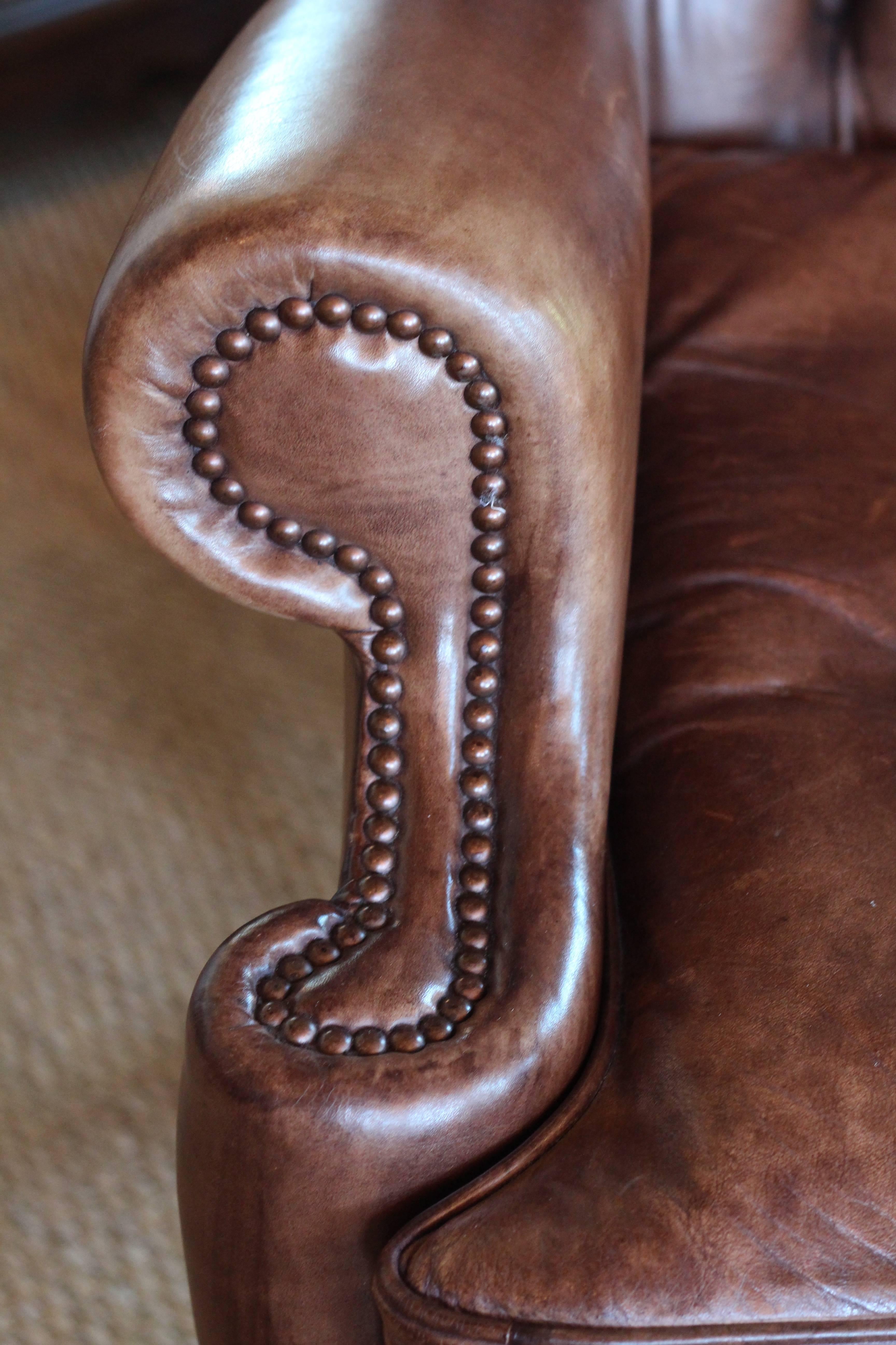 One of a pair of English wingback chairs. Finished in warm brown leather with a mahogany frame.