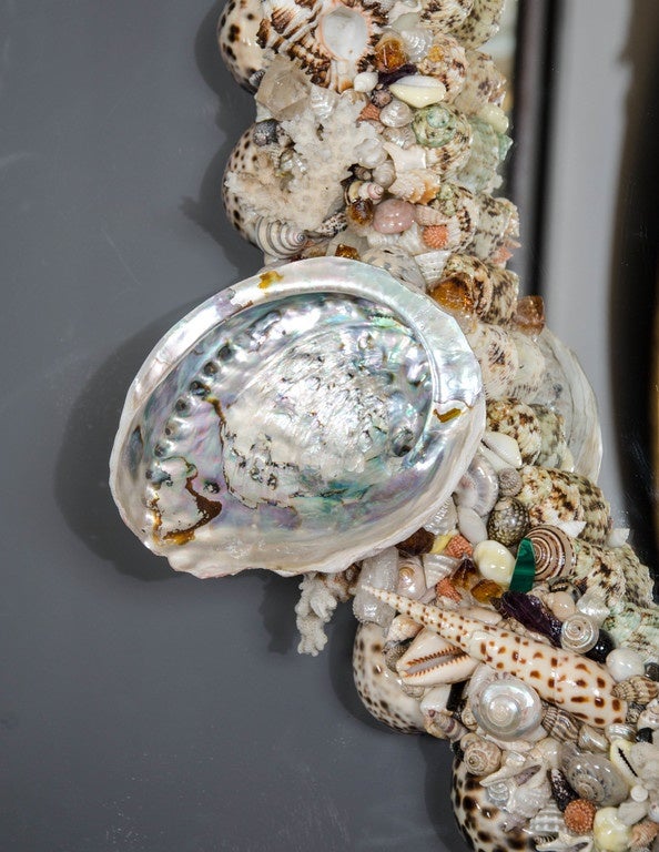 A highly ornate and decorative oval wall mirror comprised of an array of different shells including clam, conch and abalone. This mirror is a sample of the design and size, which will be priced accordingly to size if you would like something larger