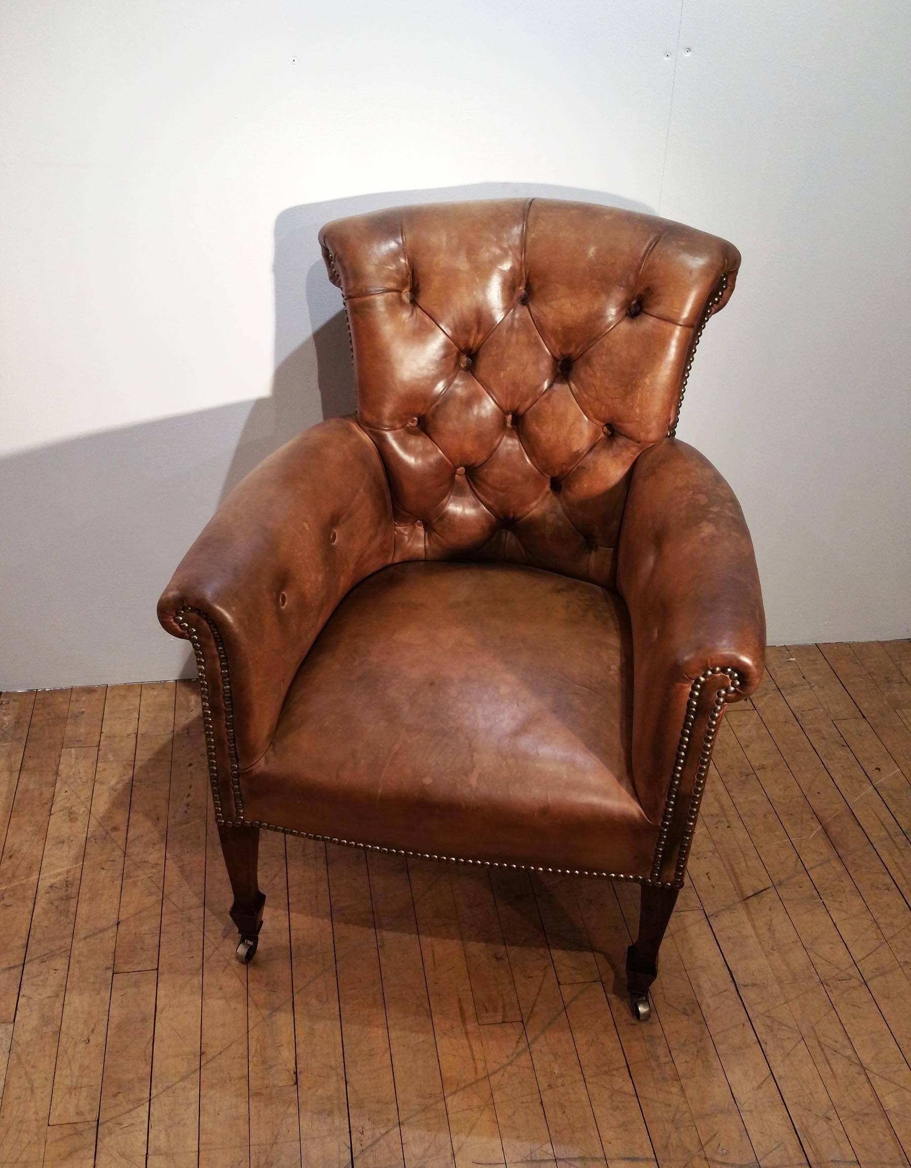 This very handsome pair of early 20th century tub chairs feature the original leather upholstery and brass castors. The chairs have a lovely scrolled back and curved arms, with deep buttoned detail and Stand on mahogany legs. Each chair measures 26