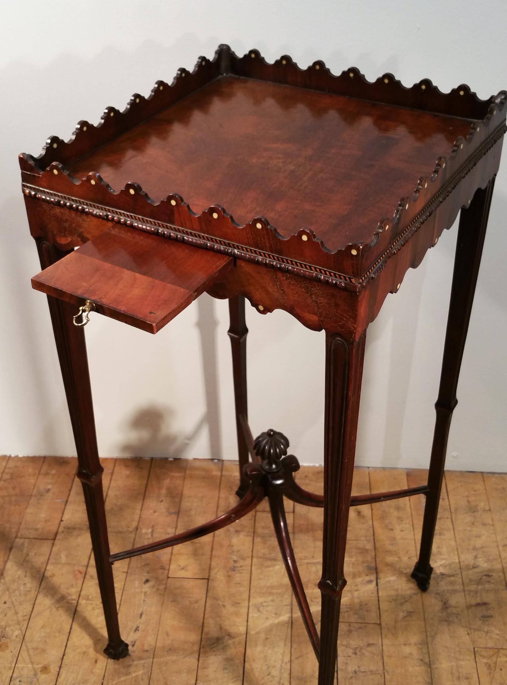 This superb 19th c. mahogany George III kettle stand is in the manner of Chippendale and features a small slide with a brass pull underneath the front apron for cups. The stand has a thin rope trim around the sides with a decorative and shaped