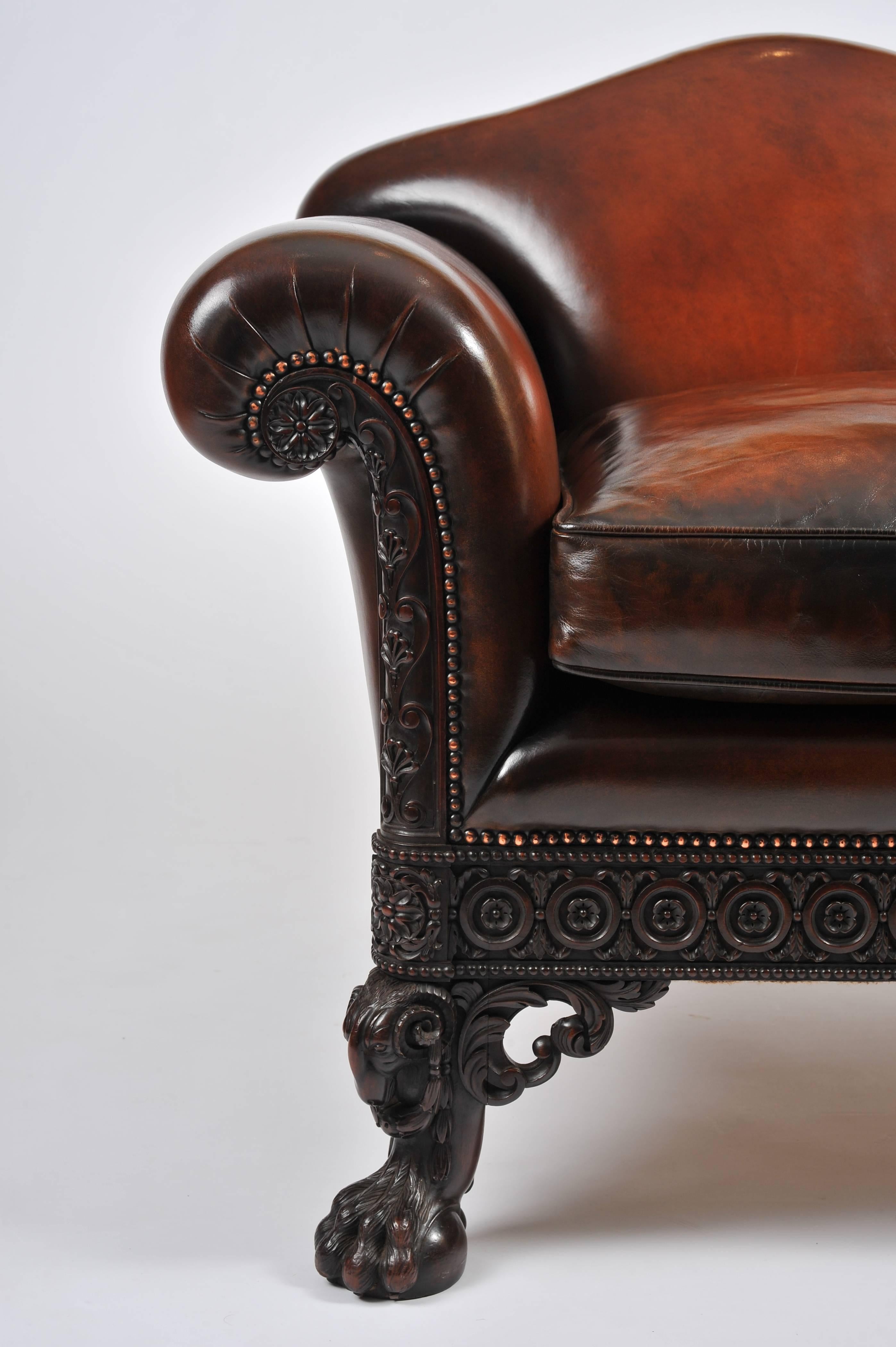 This gorgeous and superb quality leather upholstered deep armchair features a shaped back with scrolled back arms and a separate seat cushion. The carving to the mahogany base is intricate and finely detailed in design, with a circular and floral