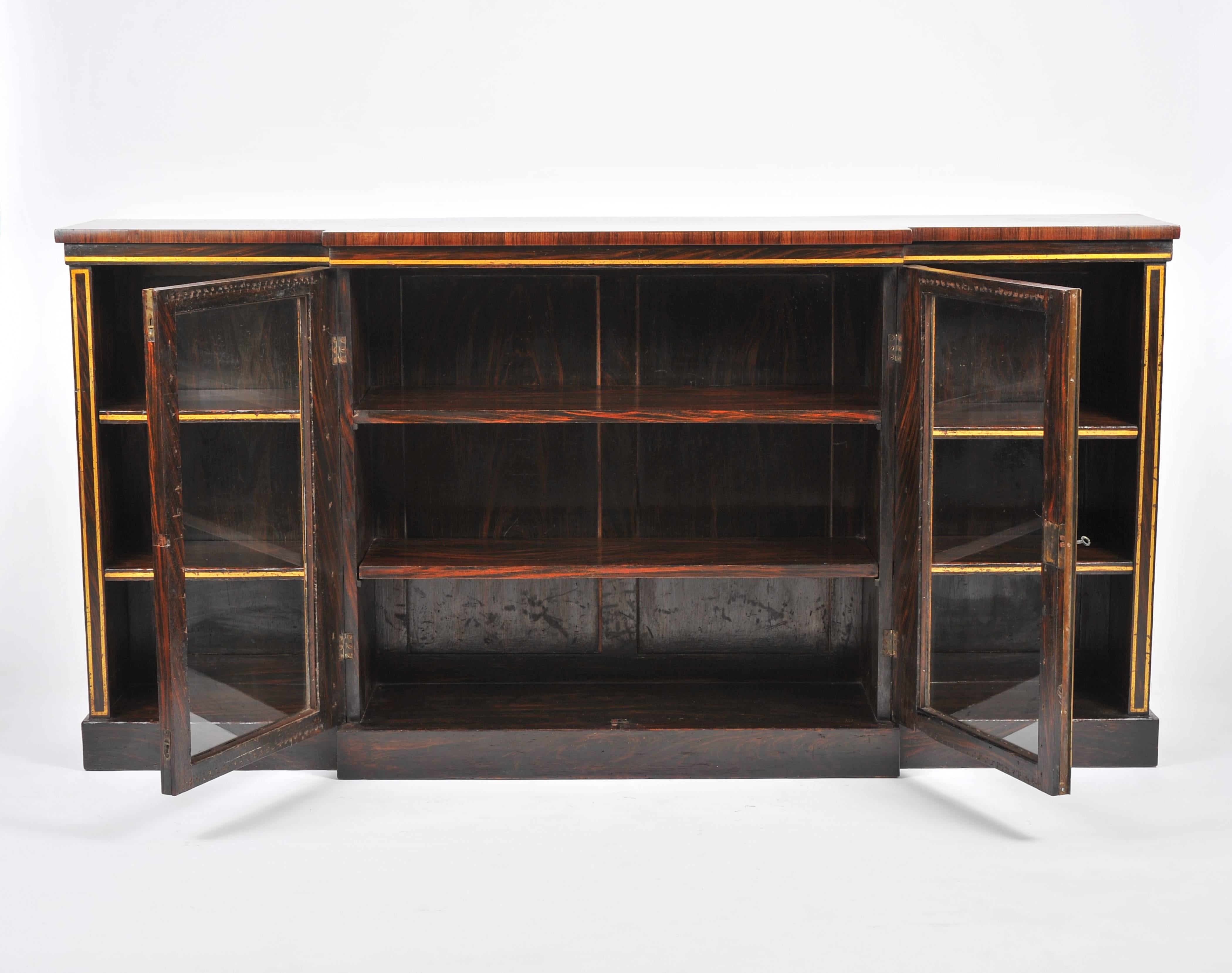 This magnificent Regency Rosewood breakfront bookcase features 2 central glass doors with open shelves on both sides. The bookcase has gilt detailing and rests on a plinth base. It measures 72 in – 183 cm wide, 14 in – 35.5 cm deep and 36 in – 91.5