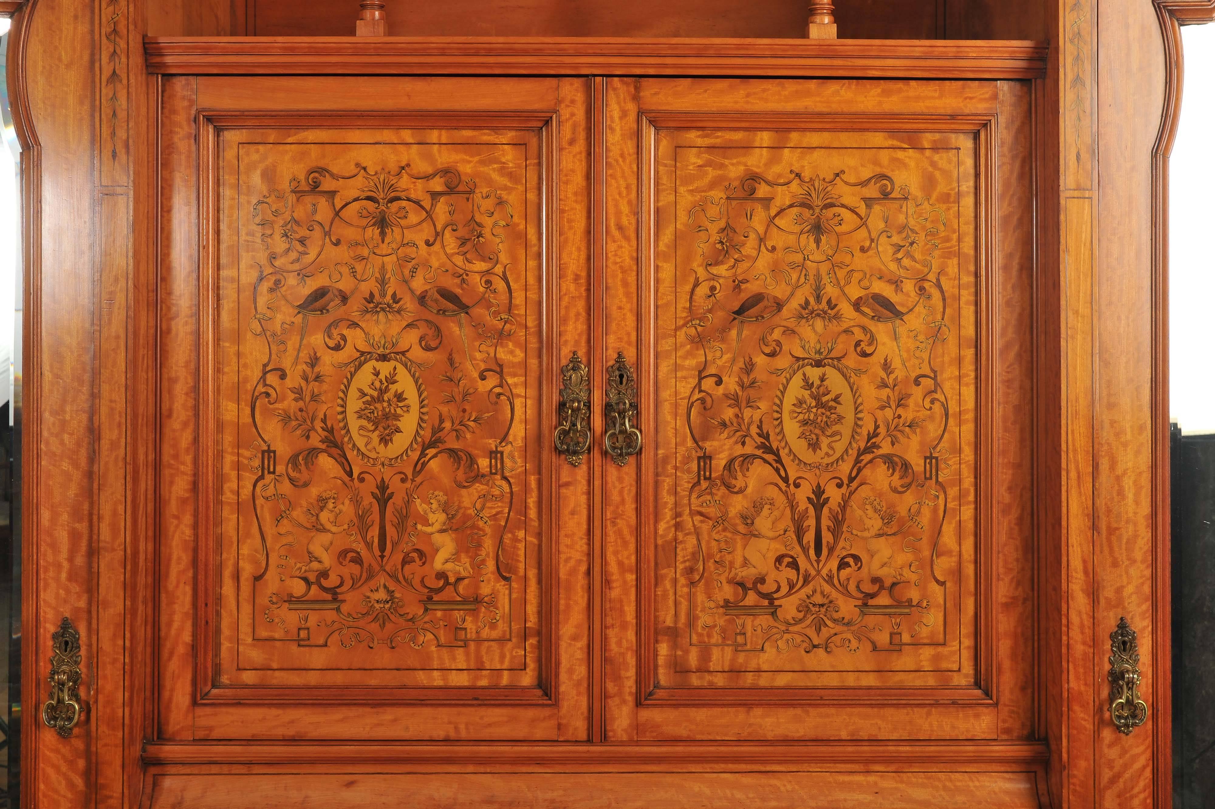 This magnificent late 19th century English satinwood wardrobe features an ornate inlay work of floral, cupid and parrot designs surrounded by swags and scrolls. The wardrobe is grand in size and of exceptional quality. Each side has hooks for