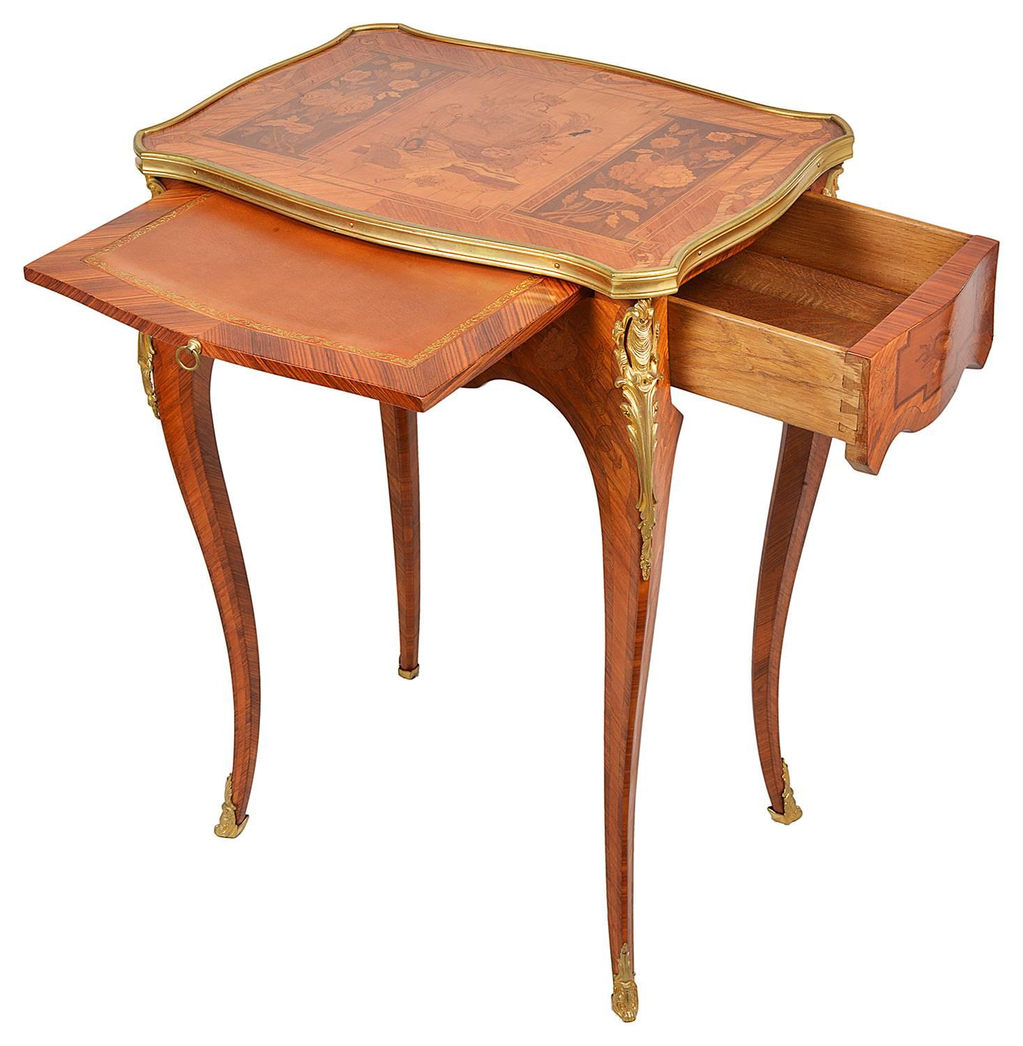 A very good quality late 19th century marquetry inlaid Louis XVI style side table. The top depicting musical instruments and floral decoration. Having a single frieze drawer and writing slide to the side. Raised on elegant cabriole legs with gilded