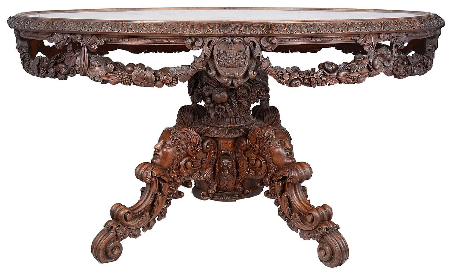A Victorian carved walnut and marble mounted centre table, circa 1860, the oval grey veined white marble top within a repeated acanthus carved edge, the pierced frieze decorated with fruiting branch swags interspersed with armorial shields, one