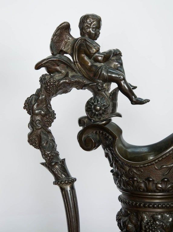 A very large pair of French bronze ewers,
in the manner of Clodion
each with tapering ovoid bodies cast with a Bacchic procession between bands of grapes and vines, the scroll handles surmounted by Winged Amorini