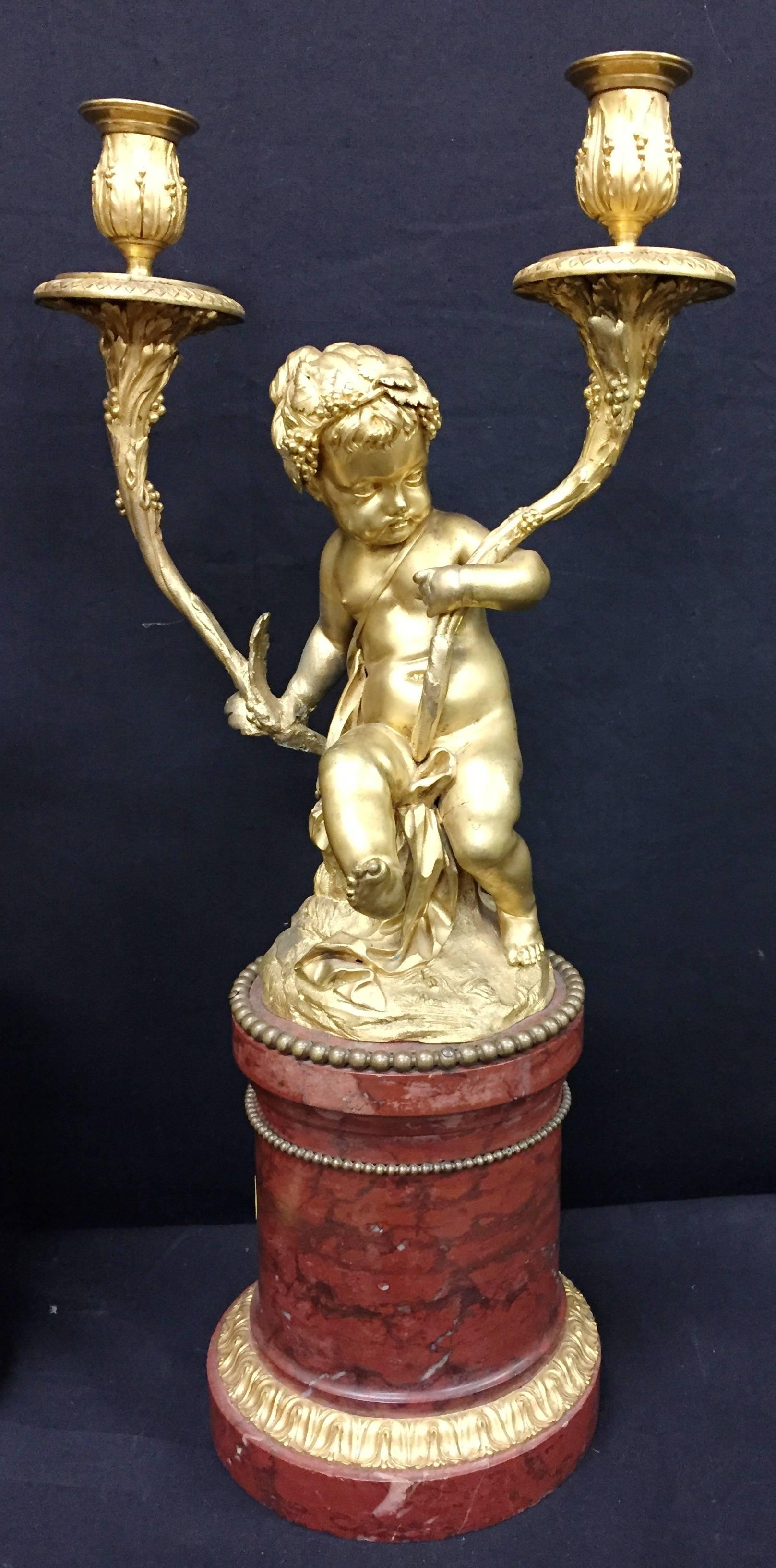 A good quality pair of French gilded ormolu and rouge marble candelabra, depicting two putti each supporting a two branch candelabra.