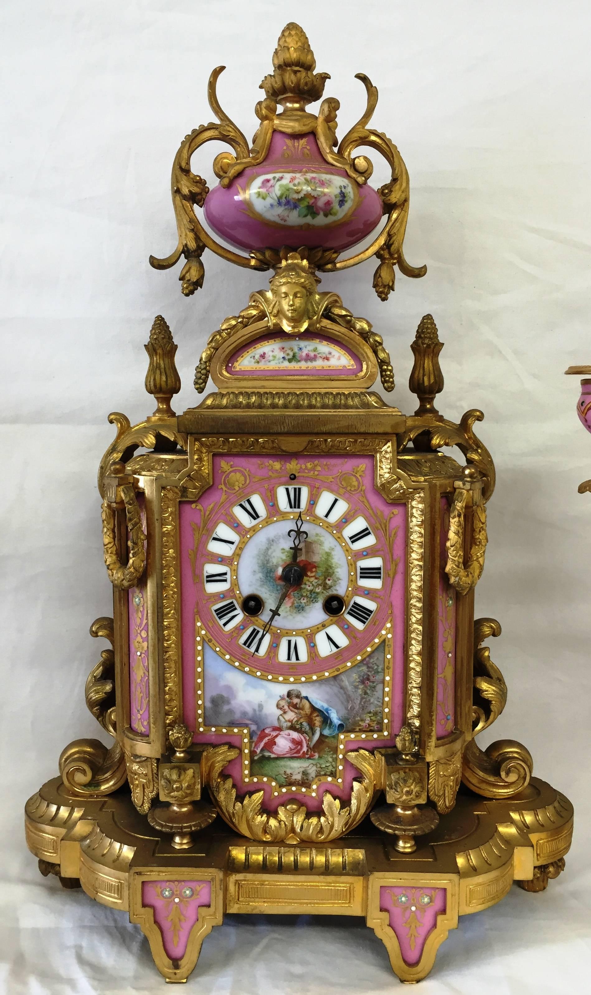 A good quality French, 19th century pink sevres porcelain and gilded ormolu clock set. Having a classical urn to the top, an eight day chiming movement. A romantic scene painted to the central panel and a pair of two branch candelabra on either side.