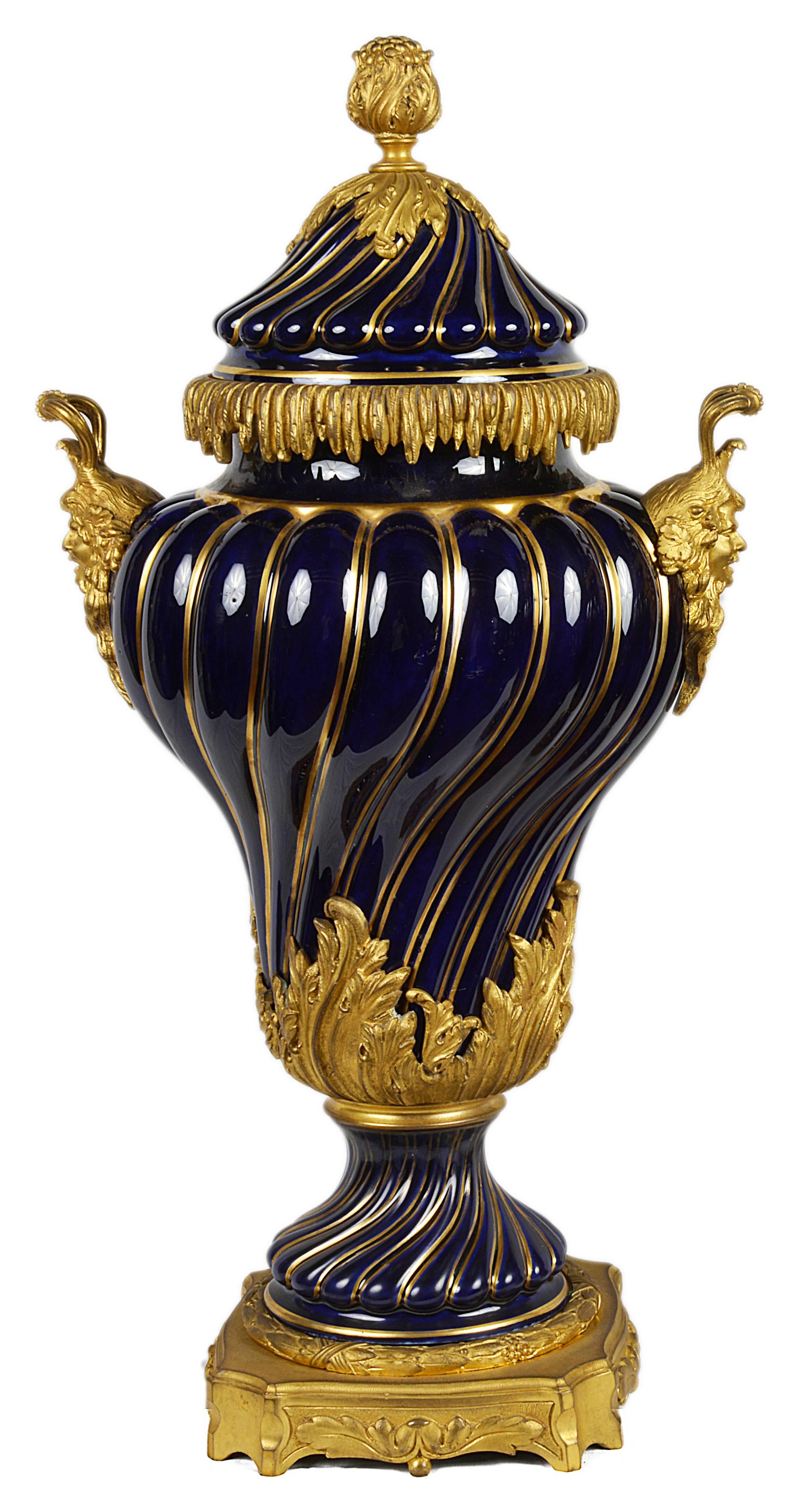 A good quality pair of 19th century gilded ormolu, Royal blue porcelain lidded vases. Each having gilded mask handles on either side and a raised and ribbed decoration with gilded lines between.