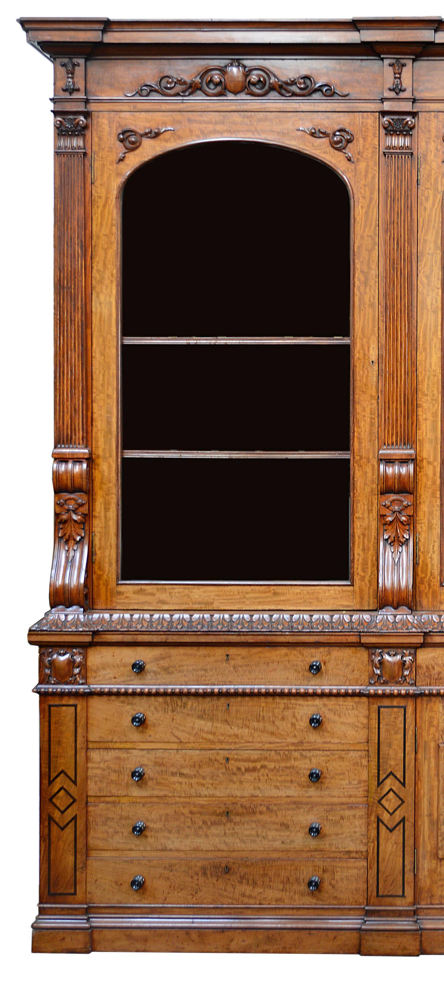 A very good quality late Regency period mahogany library bookcase. Having carved wood, fluted and ebony string inlaid decoration. Five glazed doors each open to reveal adjustable shelves. Five drawers on either side and frieze drawers above six