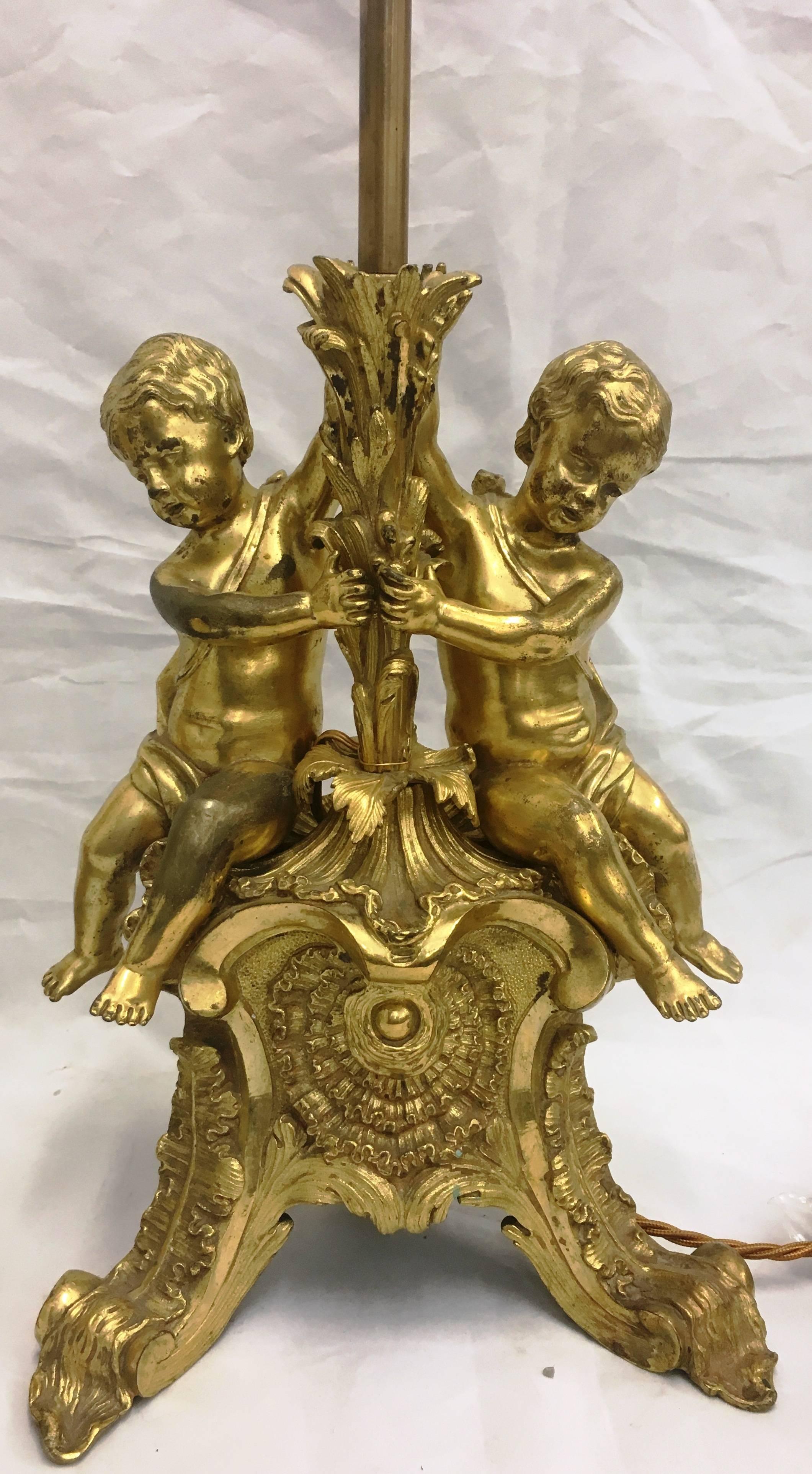 A good quality pair of French 19th century gilded ormolu lamps, each having two putti seated on a scrolling foliate base.