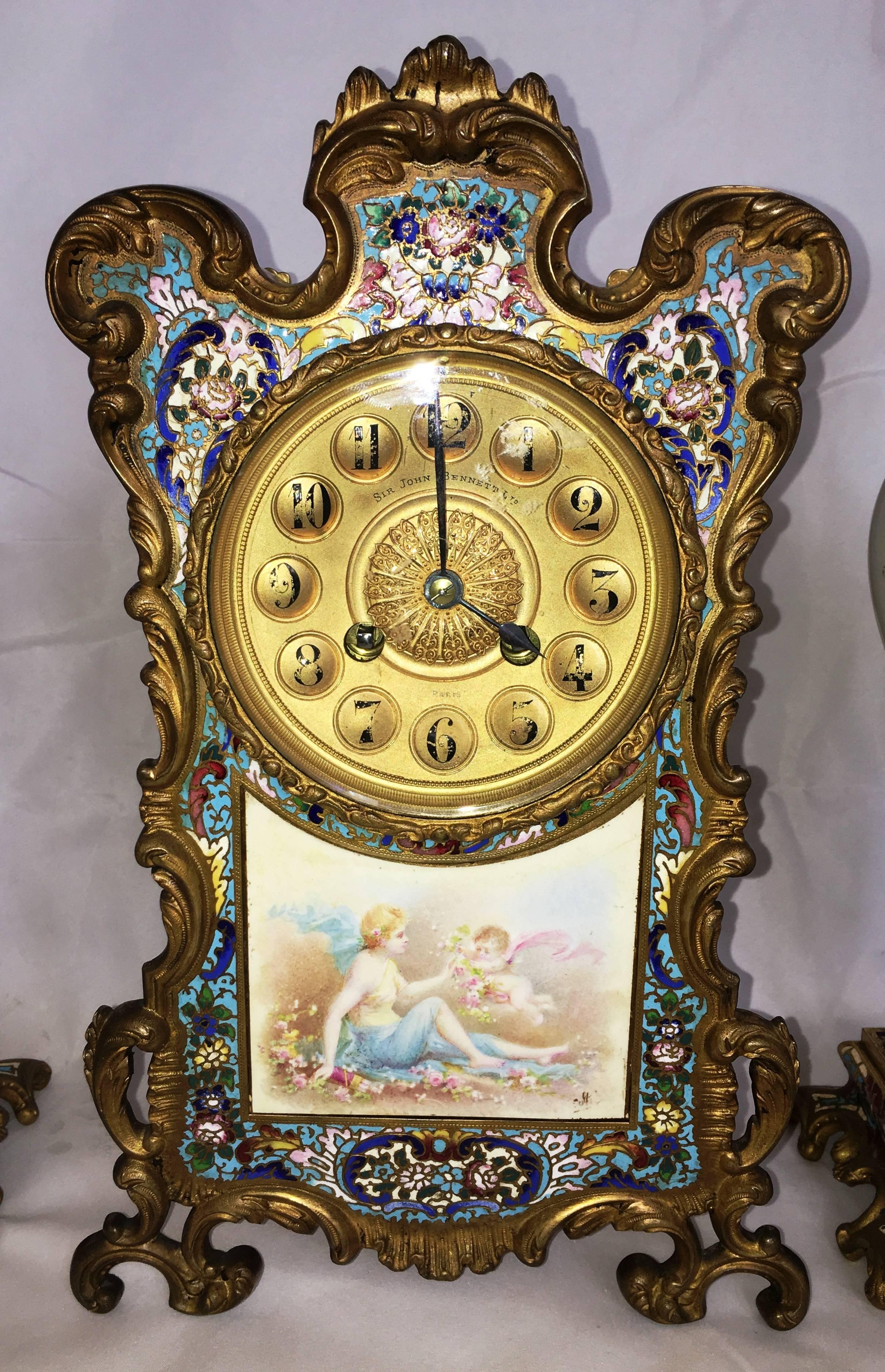 A very good quality late 19th Century French Louis XVI style Champleve enamel clock set. The clock having a classical scene of a cherub handing flowers to a young maiden. the boarder of the clock having wonderful colored enamel set in an gilded