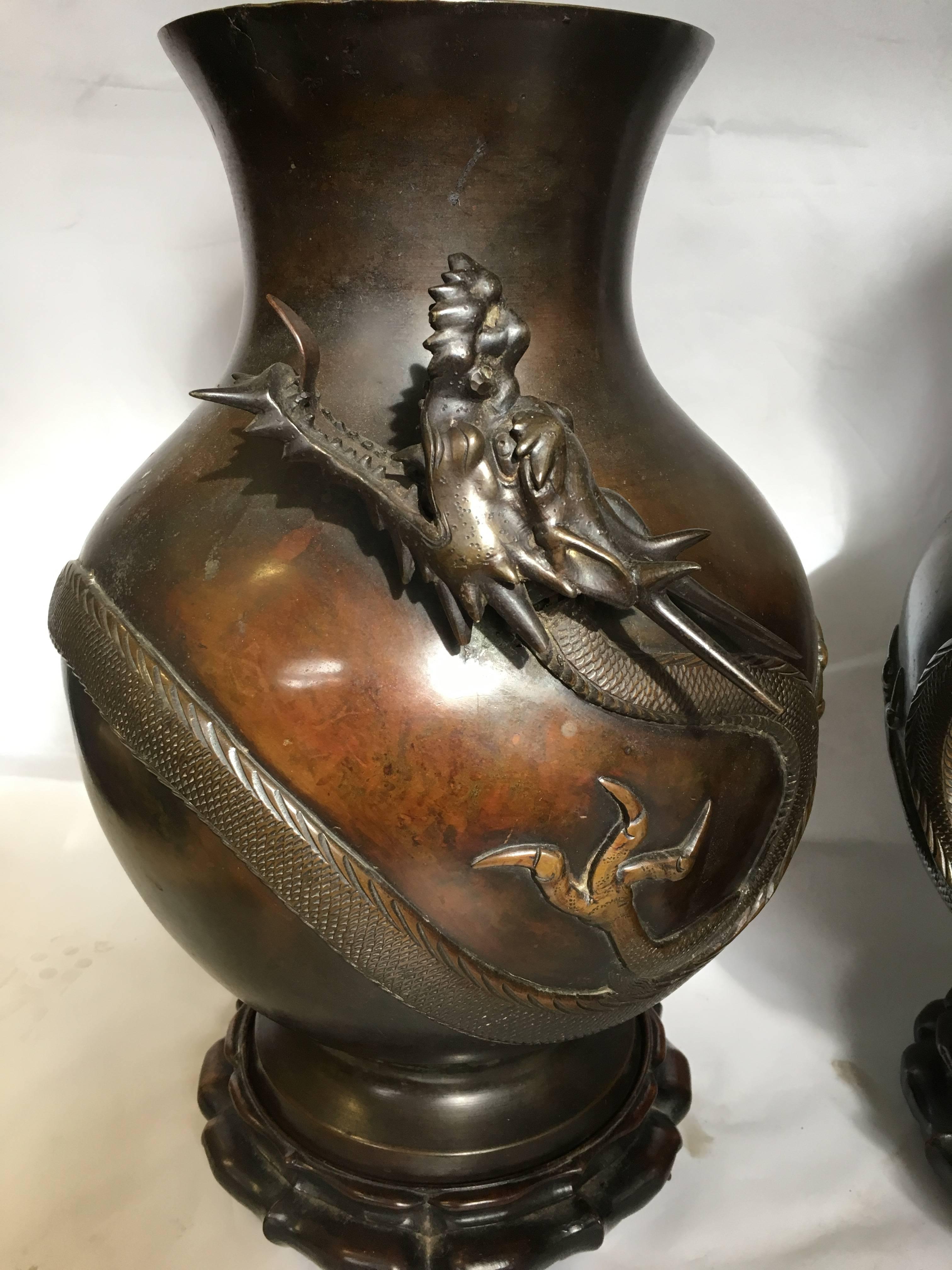 A very dramatic pair of Japanese 19th century (Meiji period 1868-1912) bronze vases, each having mythical Dragons wrapped around them, good patina and mounted on carved hardwood stands.