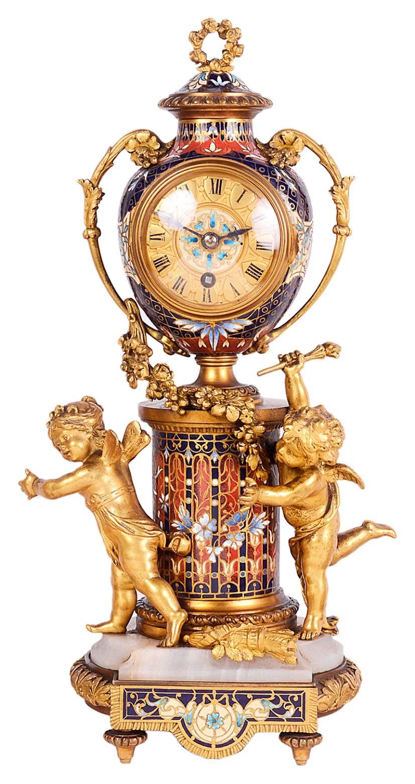 A fine quality late 19th century French gilded ormolu and Champlevé enamel clock garniture. Having cherubs playing games around the clock, which has a gilded face and Roman numerals, and a pair of matching enamel and ormolu candle sticks.