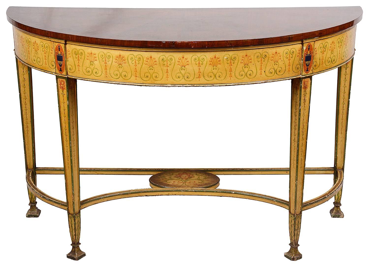 A very impressive pair of 19th century Sheraton style demi lune console tables. The tops each with radiating mahogany veneers, The bases with cream painted ground and scrolling hand-painted decoration, raised on square tapering legs united by hooped