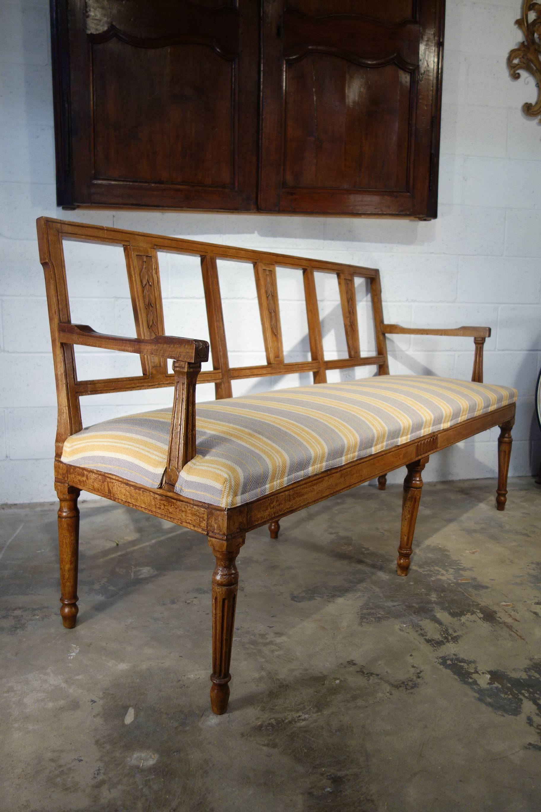 Elegant and stylish antique Italian Lombardy Louis XVI style three-seat and six-leg settee with bench cushion wrap style seat and open frame back; walnut solids with carved olive motif and scoring detail.