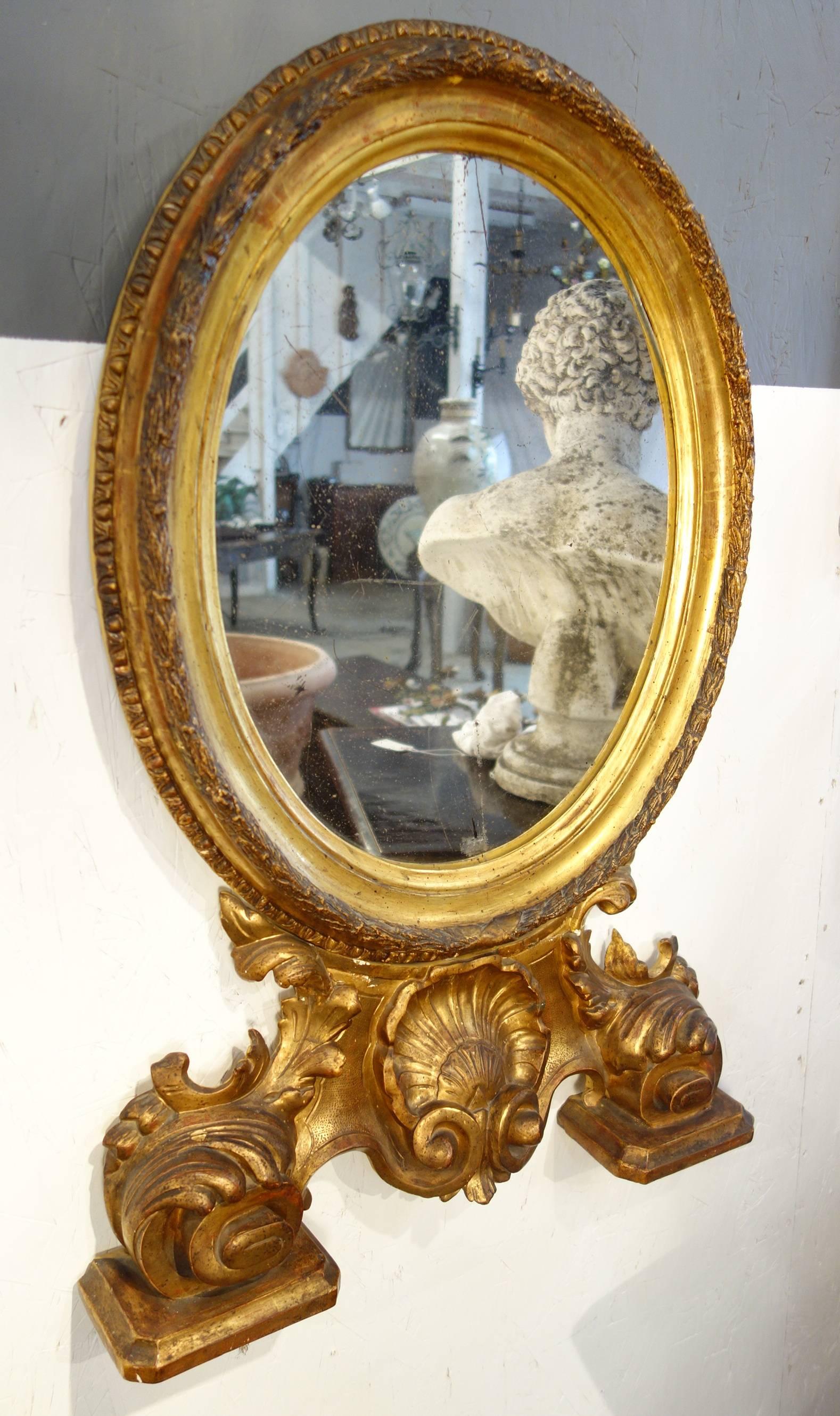 Extravagant hand-carved wood, gold gilded, burnished, moulded frame with Baroque style ornate base of leaves and central shell decoration. Original mercury mirror.

Measures: 32" H x 20" W x 4" D.