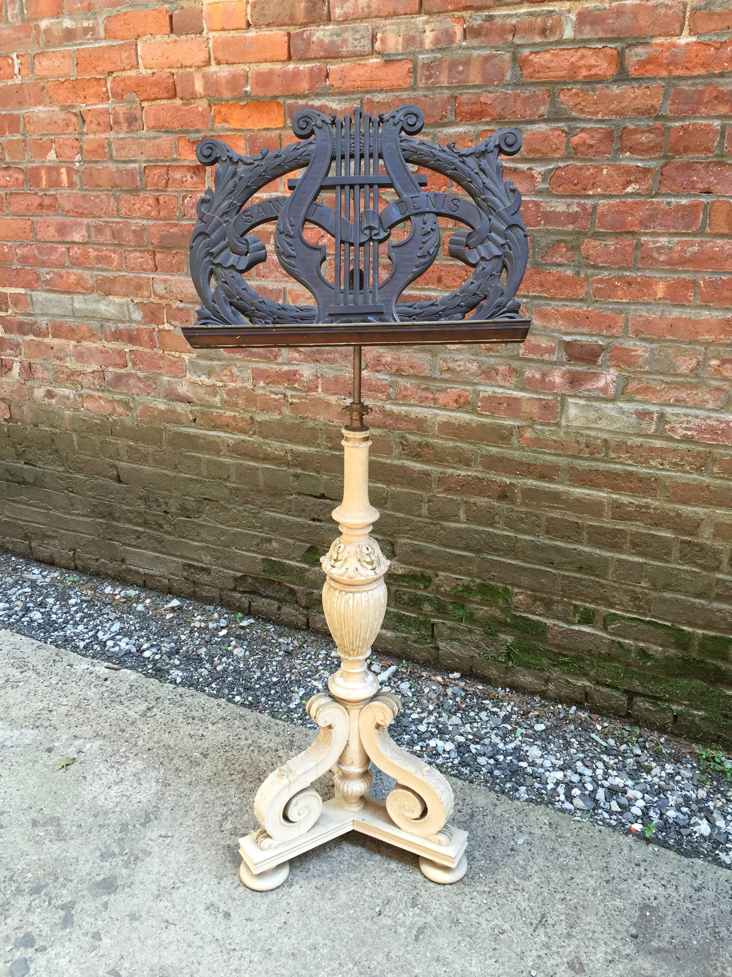 Intricately carved solid walnut music stand. Adorned with carved lyre and leaf and berry motif. Solid brass hardware for adjusting angle and height. The base retains an old white paint that is perfectly distressed and worn due to age. It is adorned