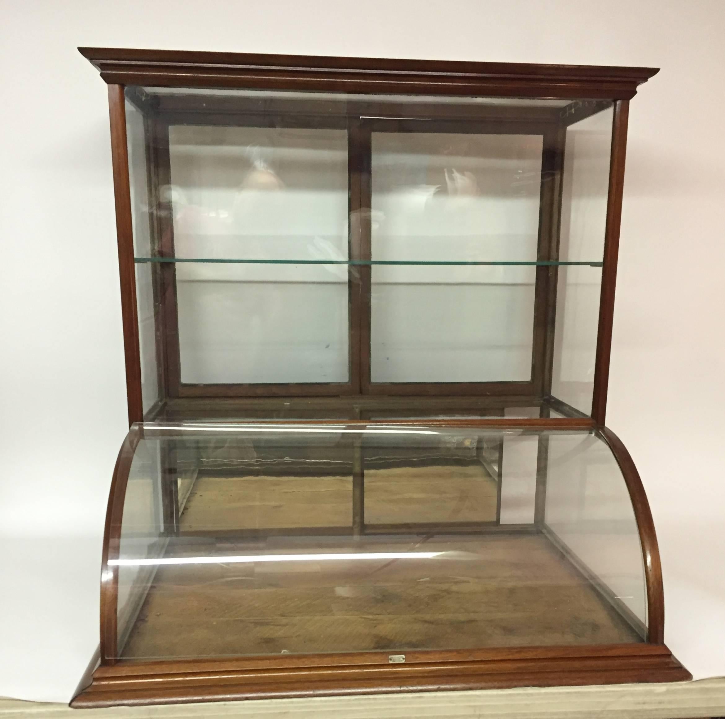 Monumental walnut curved and mirrored glass display cabinet. Tall counter top display typically found in a general retail or dry good store in the late 19th century-early 20th century. Mirrored glass sliding doors on bottom, curved glass front and