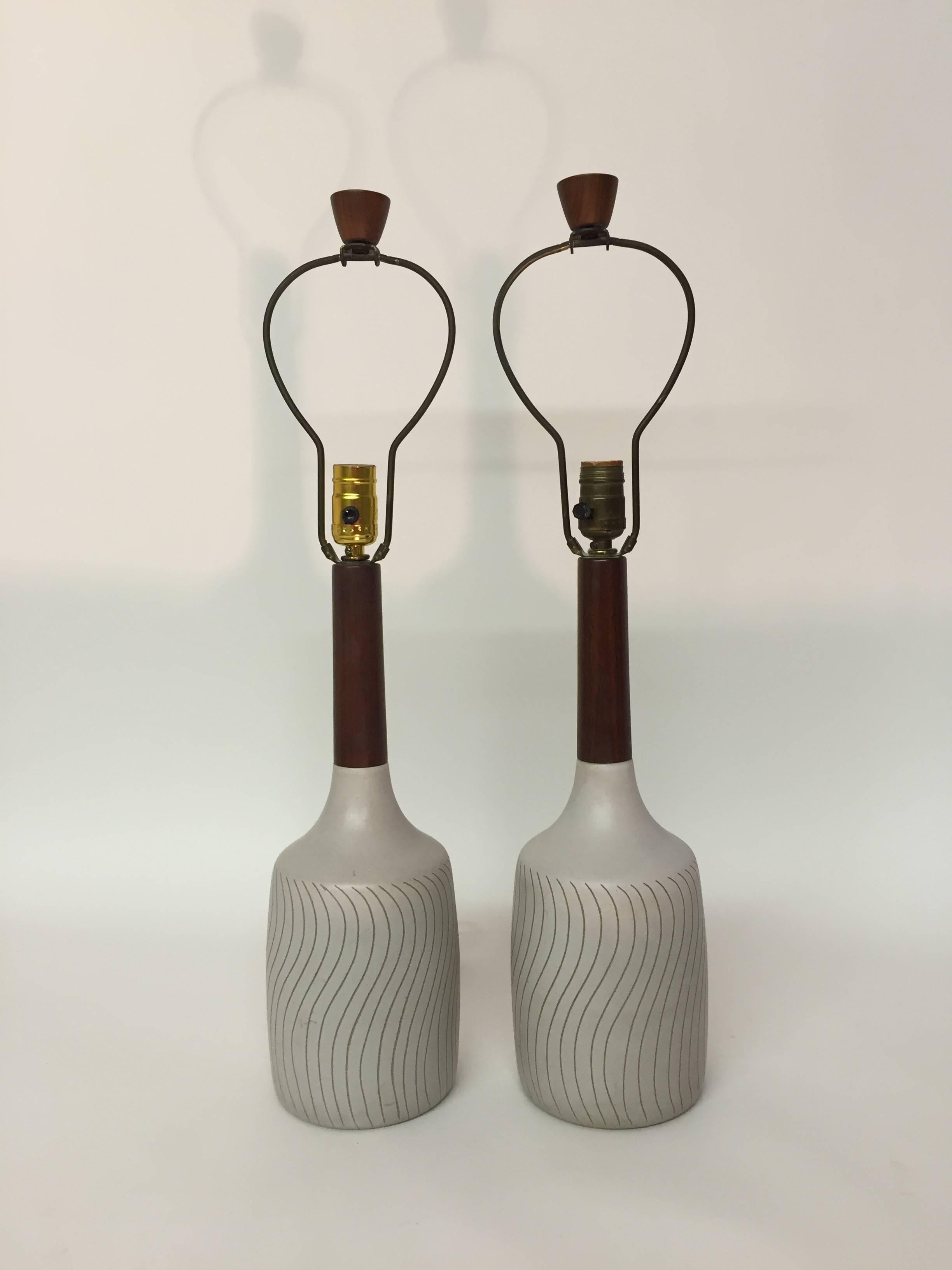 Pair of signed Martz Mid-Century Modern pottery and teak table lamps. Gordon & Jane Martz design. Decorated in a matte glaze with incised wave pattern. Overall height is 26.5" high. Original teak finials and shaft. Pottery measures