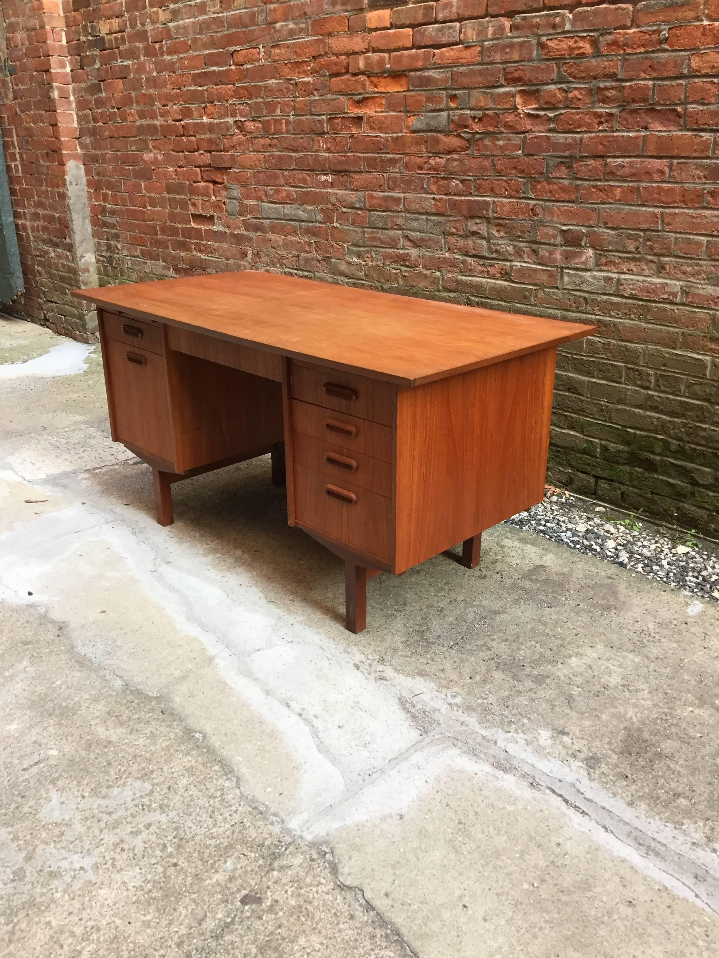 Beautiful seven-drawer teak Danish desk. Finished on all sides and has to pull out surfaces. The left hand side of the desk contains a top drawer with small dividers and the larger bottom drawer is for hanging files. Very nice original condition,