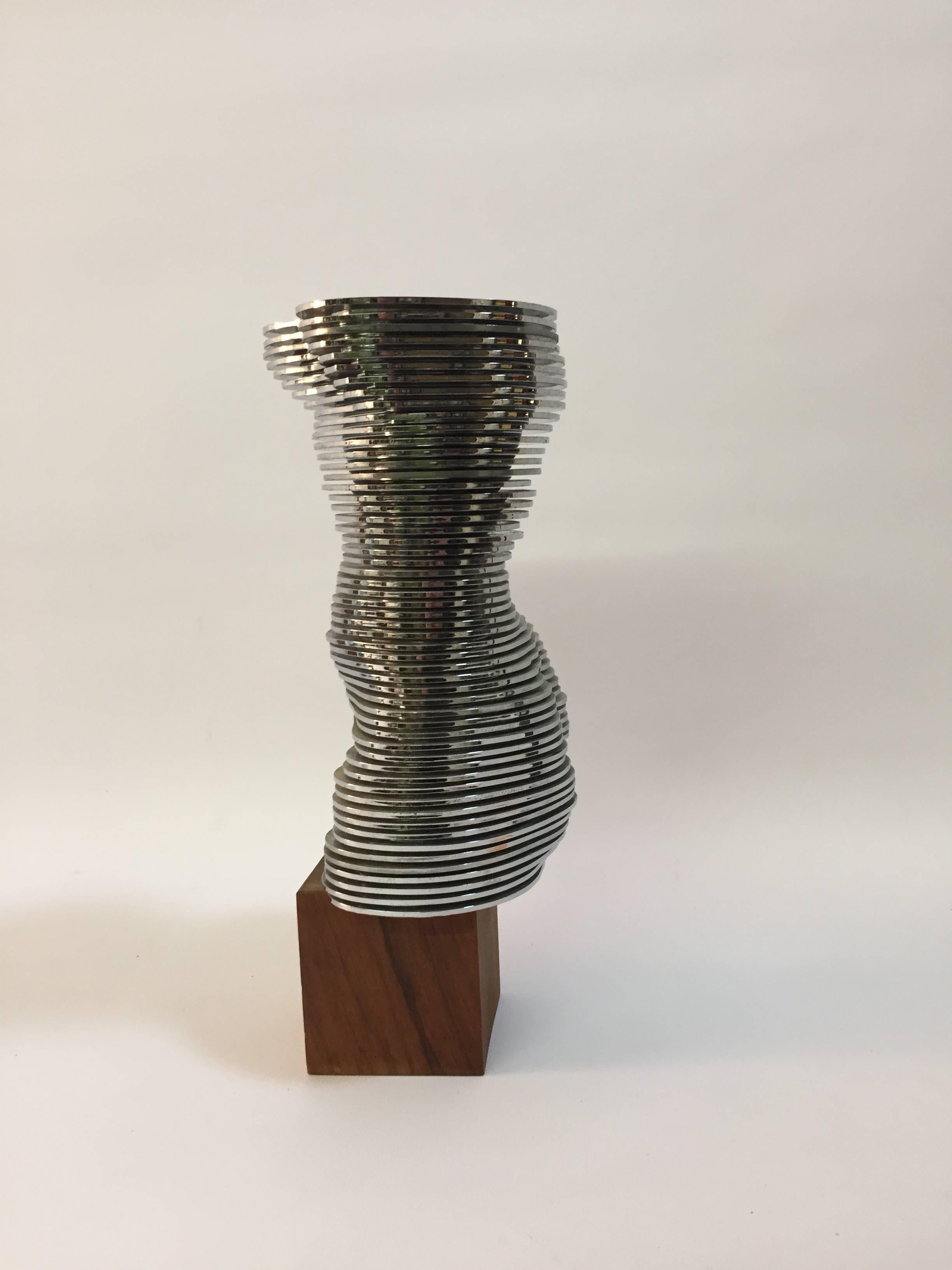 Standing on a walnut cube base are multiple stacked mirror finished plastic discs that form a truncated curvaceous female torso. Each disc pivots on a rod and can be moved to create a different version of the nude. Truly odd and special, circa 1970.