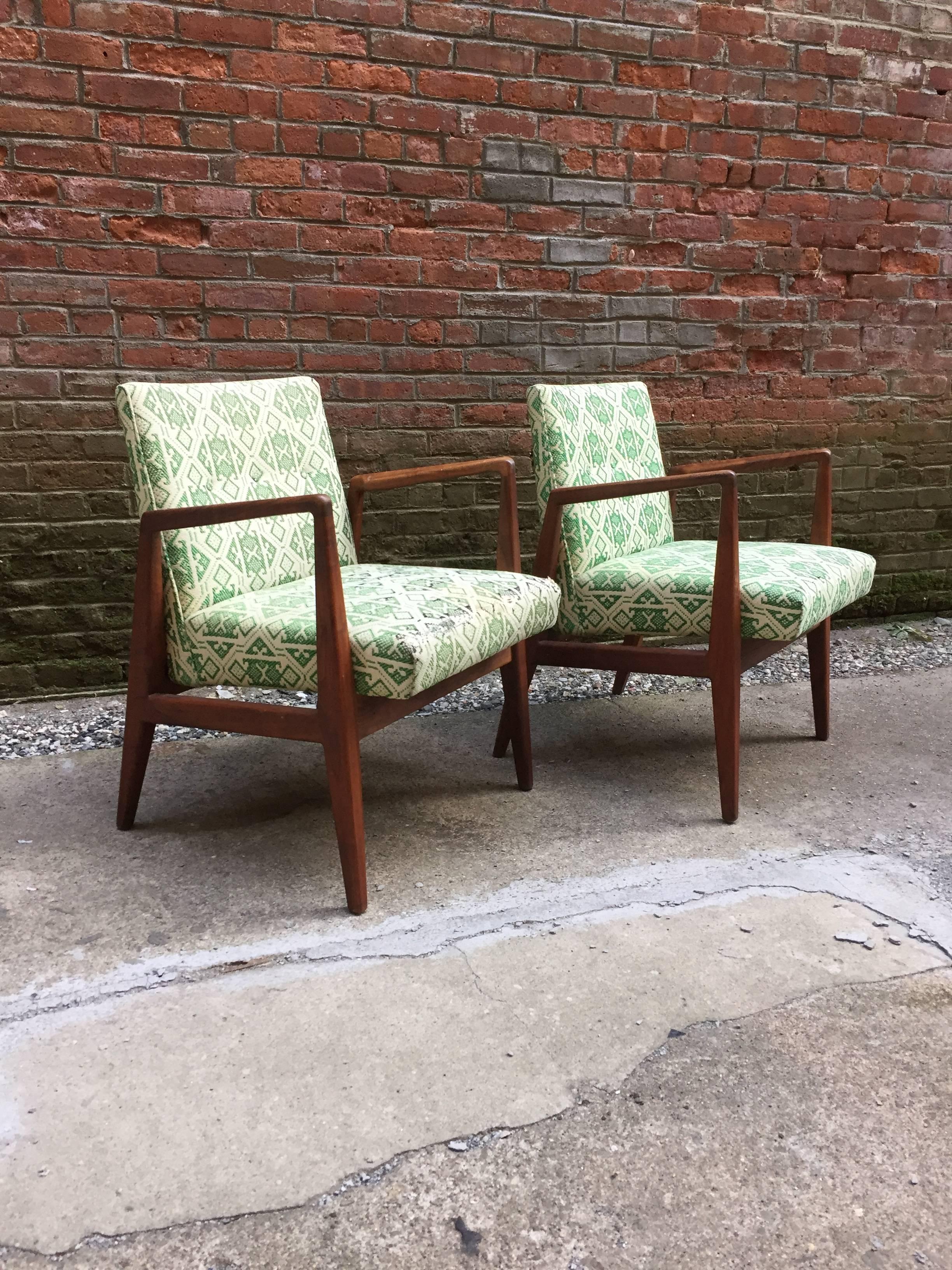 Pair of walnut framed and upholstered armchairs designed by Jens Risom. Sharp and linear.  Oiled walnut frames are in very good, original condition. Period 1960s upholstery. Both chairs are signed underneath.

Re-upholstery suggested.