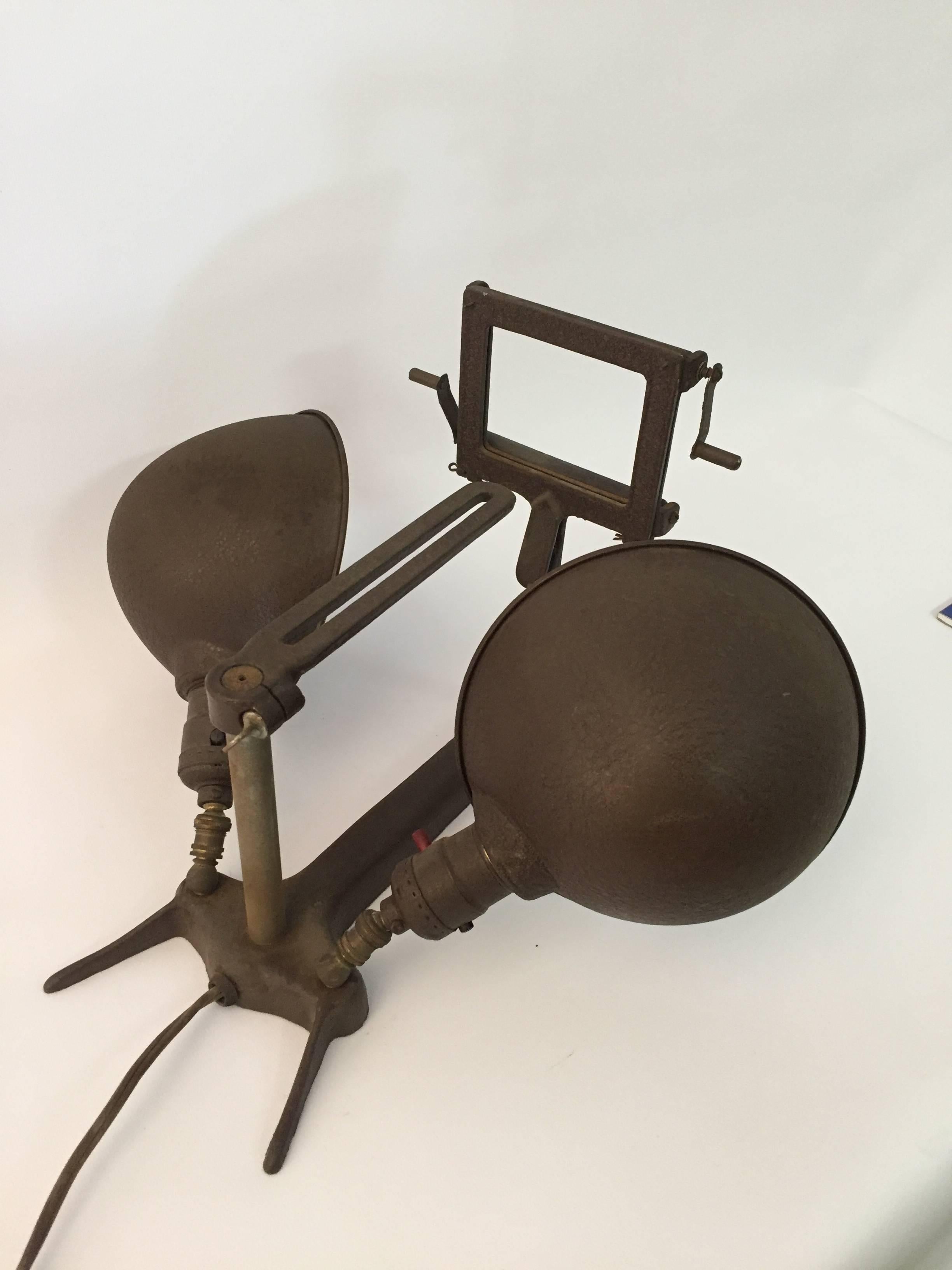 It's just an oddity of a lamp. Powder coated in olive drab this two headed lamp features a little slide screen for viewing or projecting images, adjustable shades and small wood rollers. It's meant to be placed on a flat surface for viewing