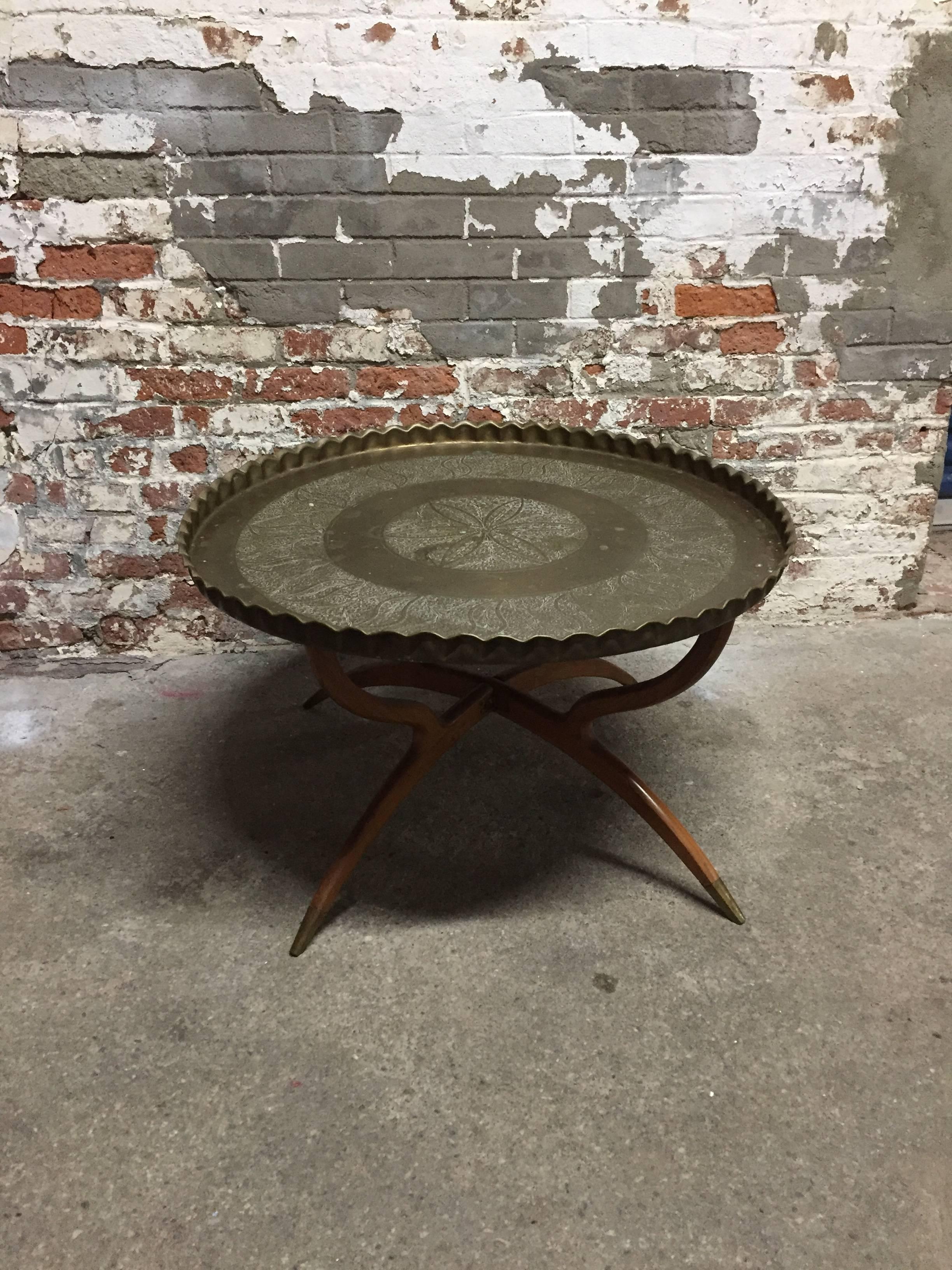 Ruffled edge hand-hammered and decorated brass tray table with folding base. Tapered wood legs ending with brass sabots. Decorated floral and scrolled tray with old mellow patina, circa 1960-1970.

Measures: 33.13