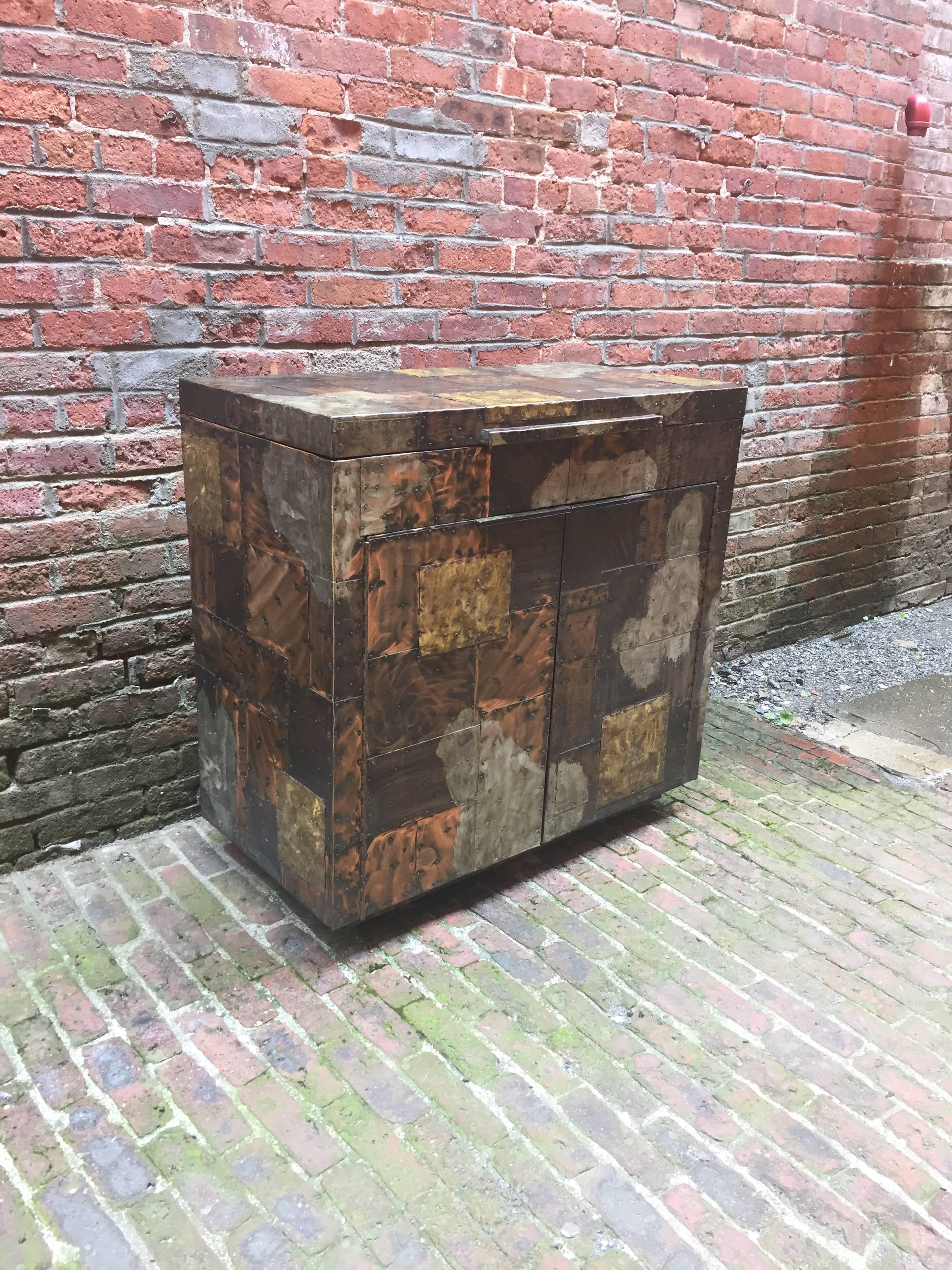 Designed by Paul Evans for Directional. Patchwork mixed metals cabinet consisting of Copper, Brass and Pewter. Black interior with flip-top and two cabinet doors with shelves. On casters, circa 1971.

Measures: 36.25