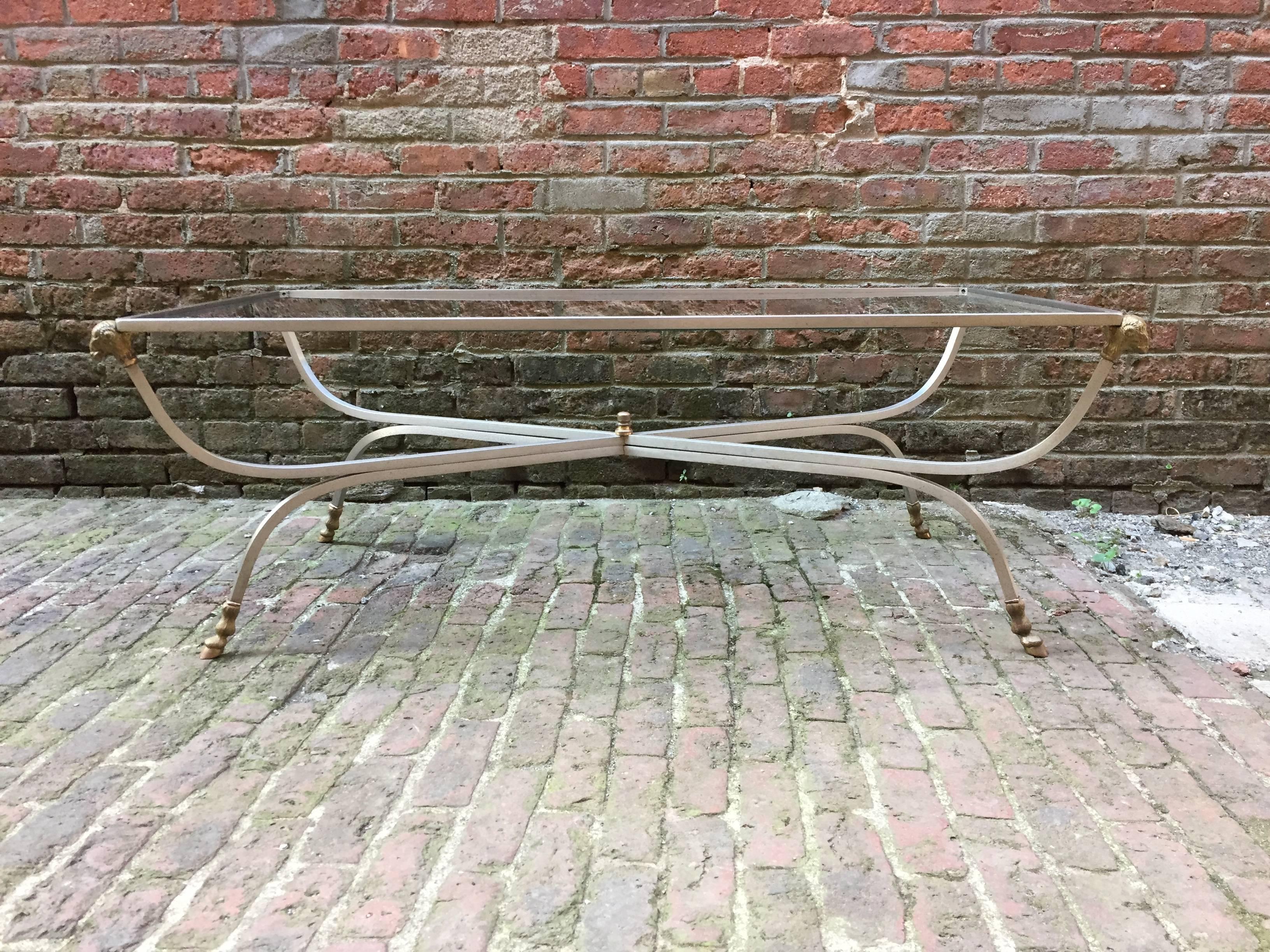 Elegant brass, steel and glass coffee table in the manner of Maison Jansen. Brass ram's head corners and cloven hoof feet. Signed, Italy, under foot. Original glass, circa 1970.

Measures: 17.5