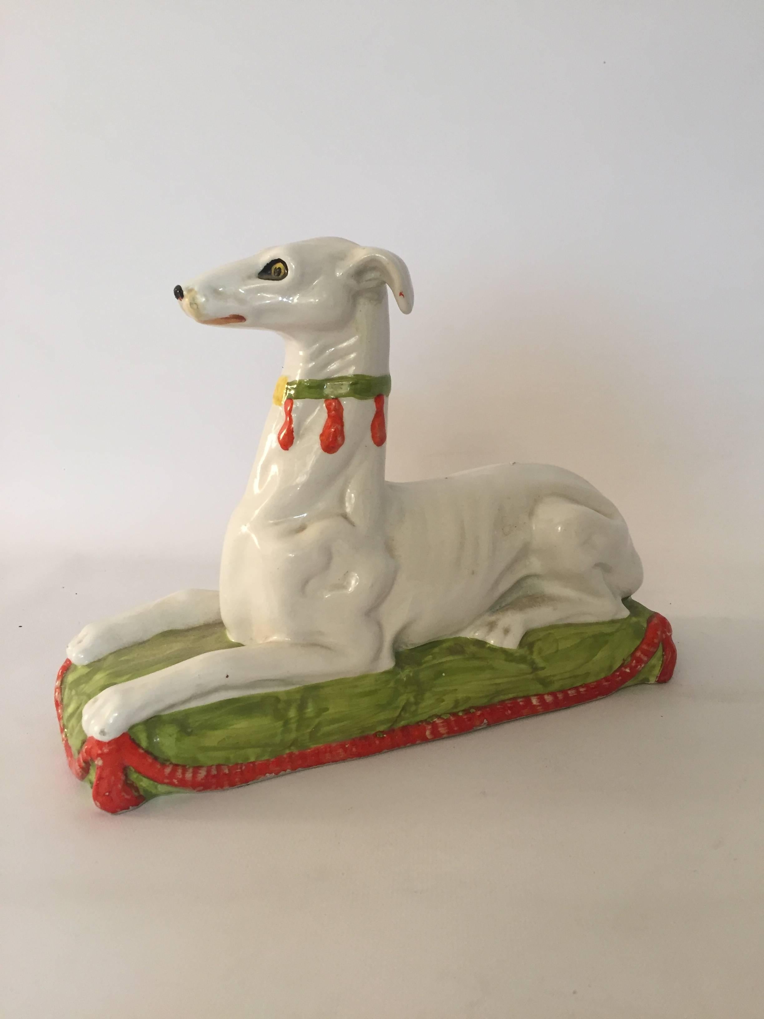 High glaze ceramic hand decorated Whippet, circa 1960. Probably Italian in origin, but not signed or marked on the bottom. This austere dog is perched resting on a green pillow base with red swagger tassels. Very good, original condition with some