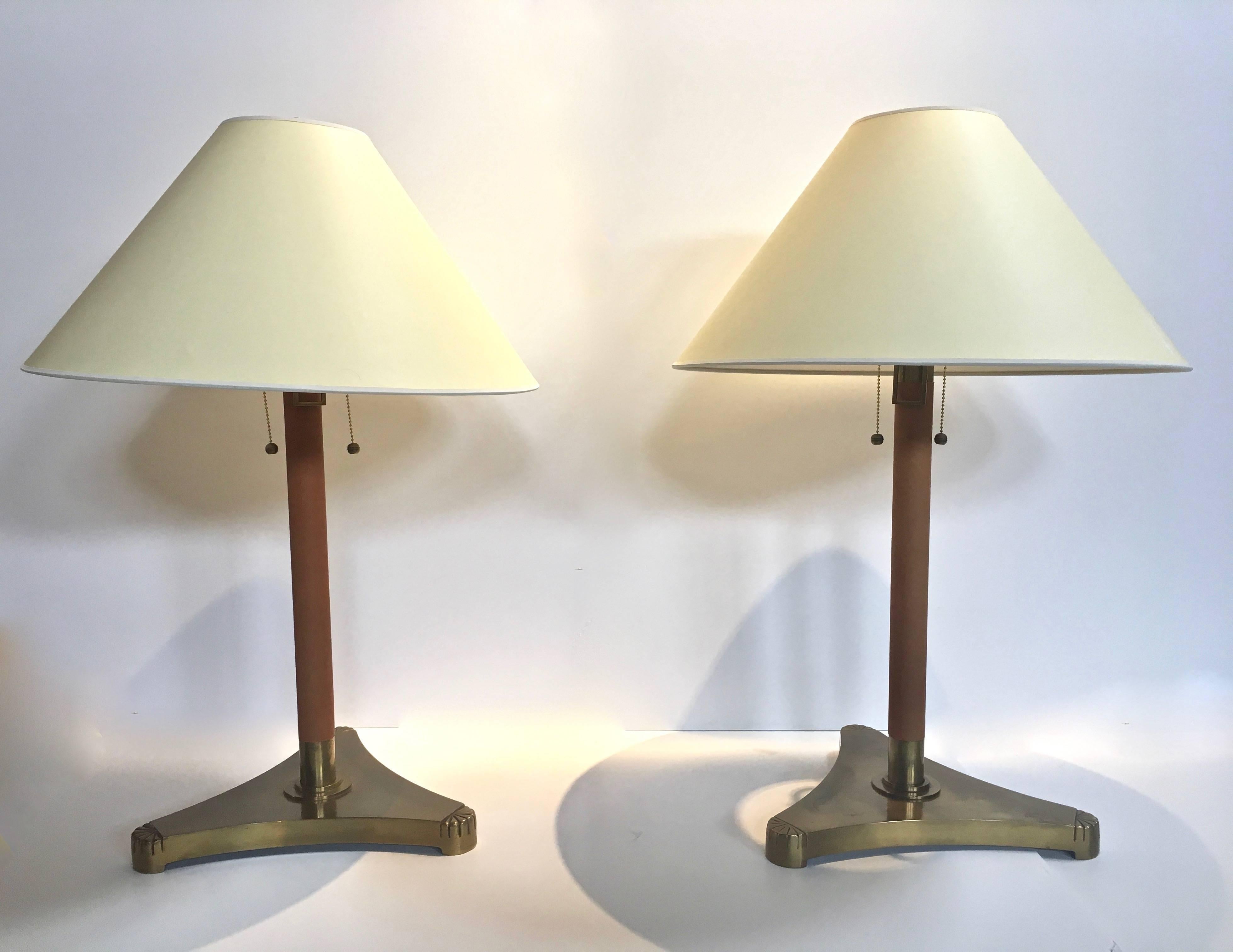 Unusual pair of extendable brass table lamps, clad in saddle stitched tanned leather, in the manner of Hermes or Adnet. Brass ring near neck of lamp, flips up releasing the brass neck of to lamp, to extend up or down 5 inches, thus creating a