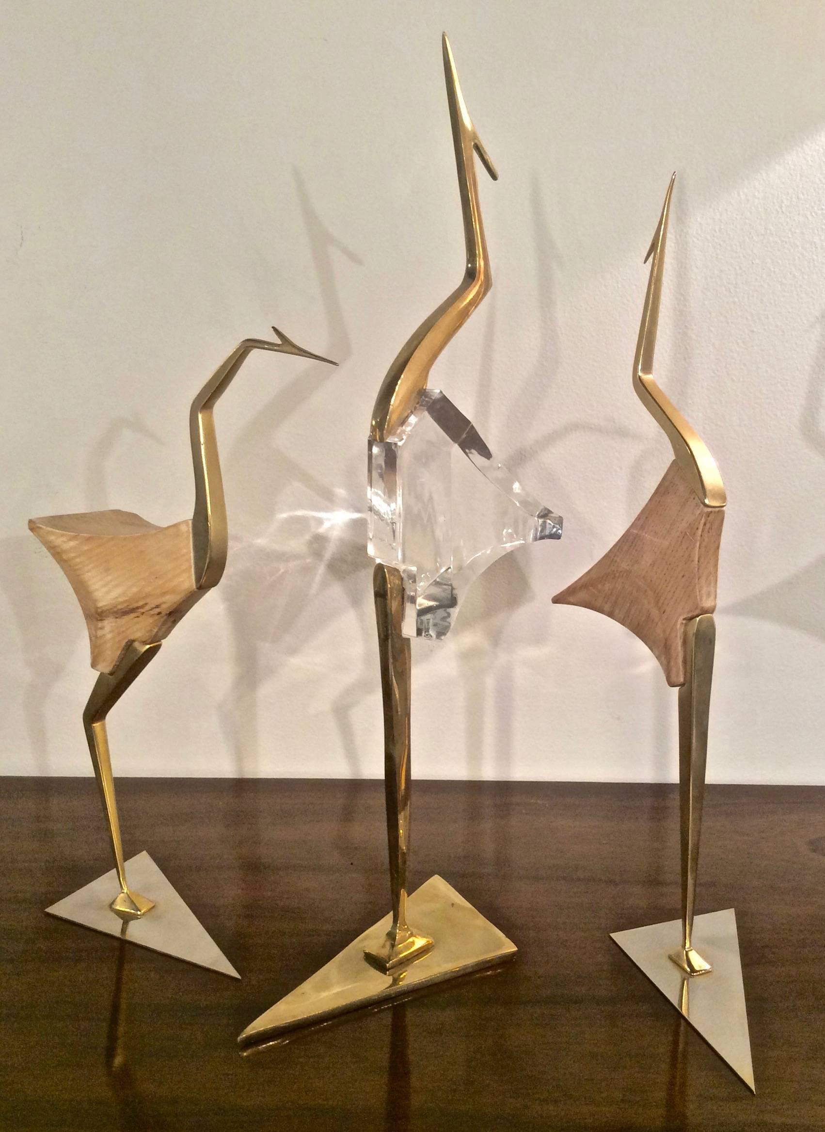 Three modernist egrets or cranes, two in brass with wood block bodies and the third larger on from brass and Lucite.

Wood crane looking up: H 17.5