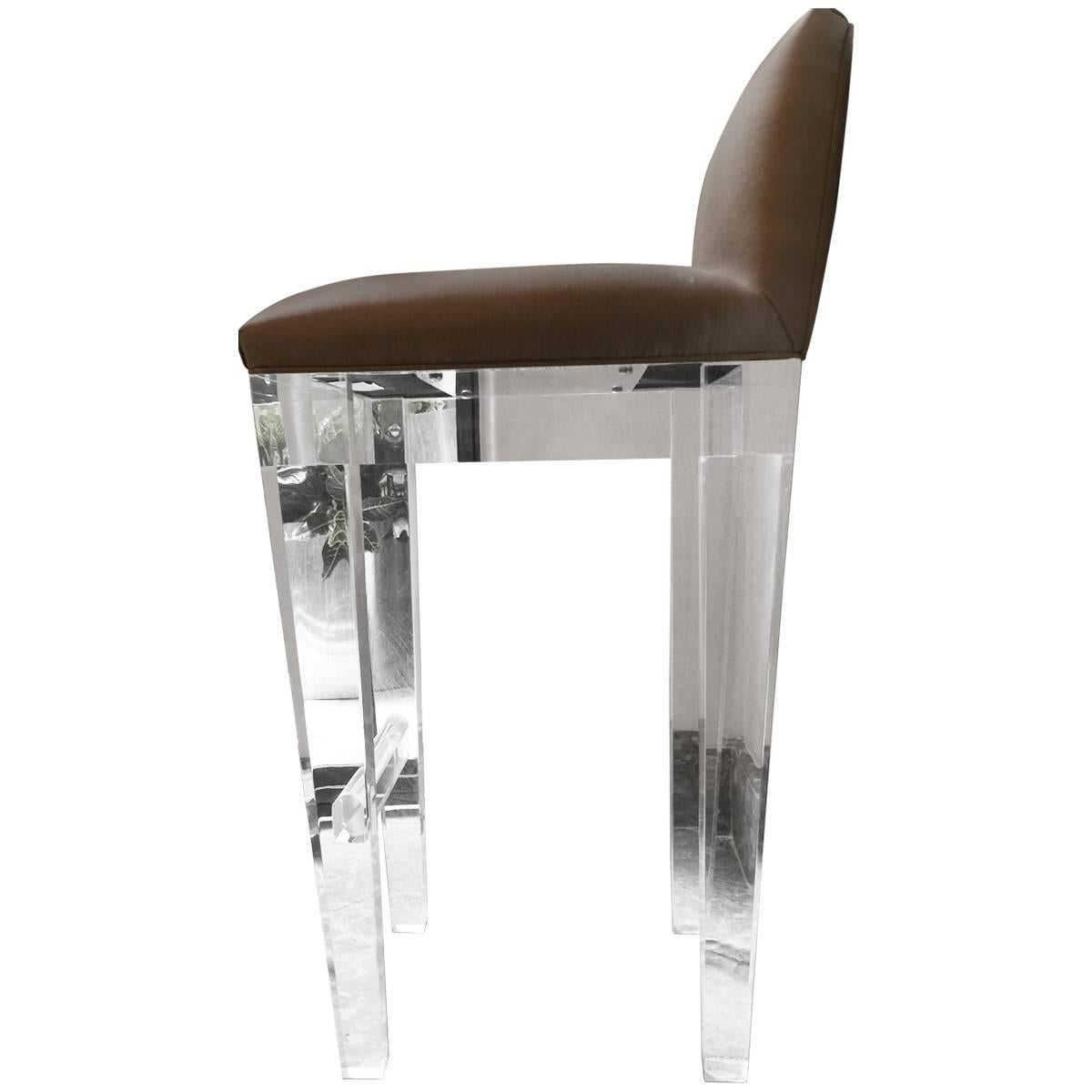 Seriously stunning set of four upholstered Lucite bar stools. Crystal clear tapered Lucite legs, and Lucite footrest. The seats are upholstered in a neutral silk (a few small blemishes pictured) these chairs are solid and heavy, and glisten like