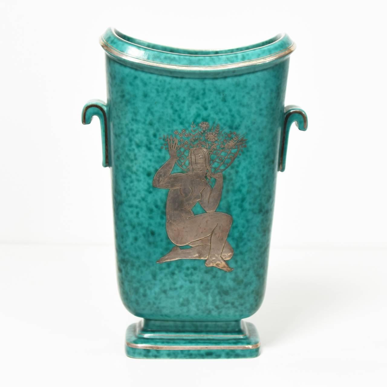 Swedish Art Deco ceramic vase by Gustavsberg with a central silver motif of a kneeling woman bearing a panier of flowers on a sea-green background.
Inscribed to base in silver: Made in Sweden or Gustavsberg /
Argenta / 1209 /BA.