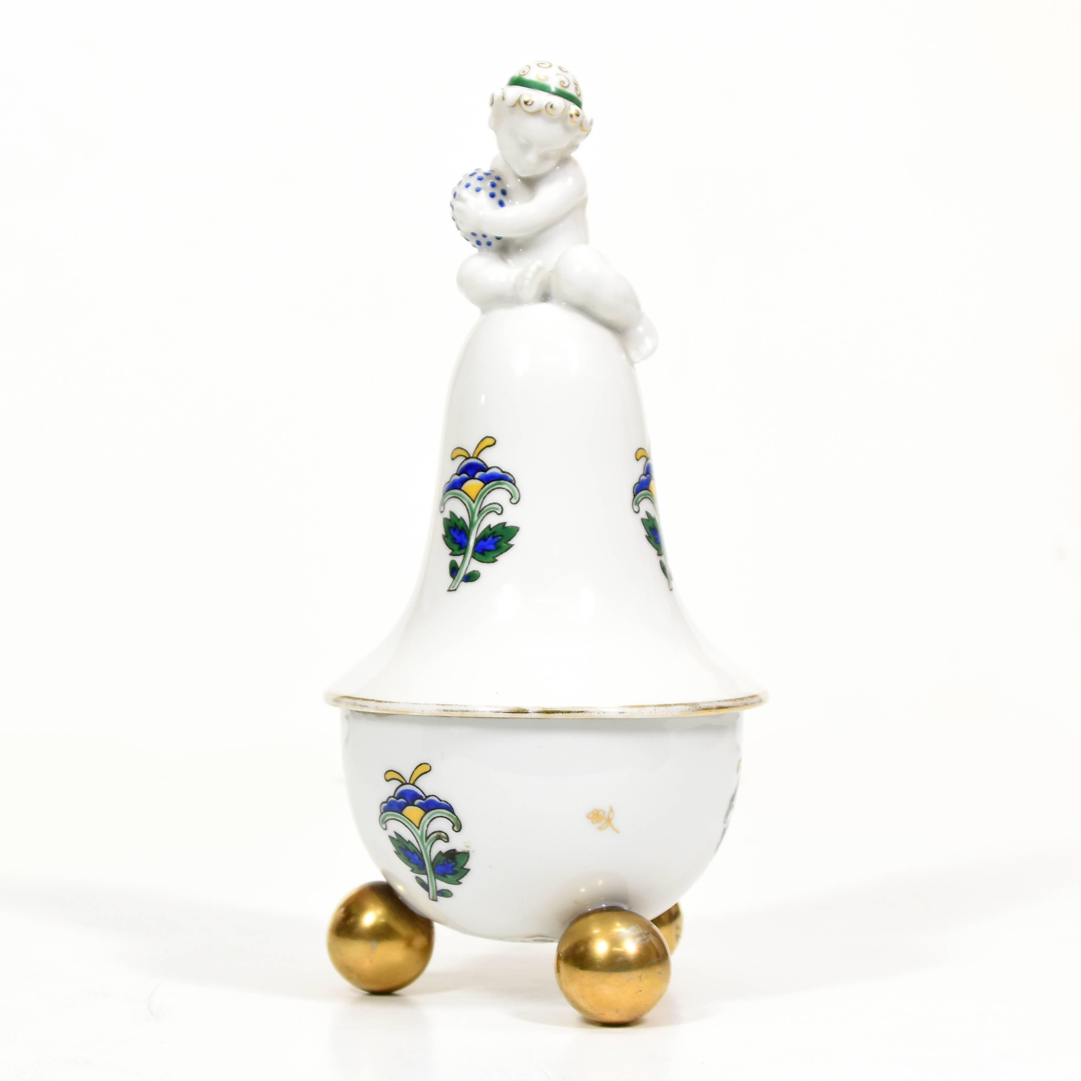 A Sucessionist lidded porcelain box featuring a Cupid, manufactured by German porcelain company, Porzellanfabrik Fraureuth (1865-1926). The piece features a large floral motif, favoured in German design of the period trimmed in gilt with gilt