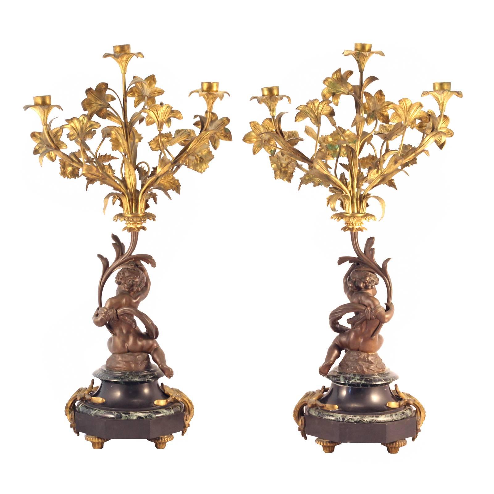 A pair of late 19th century Louis XVI style candelabra, featuring a marble base, cast bronze putti and gilt floral branches.