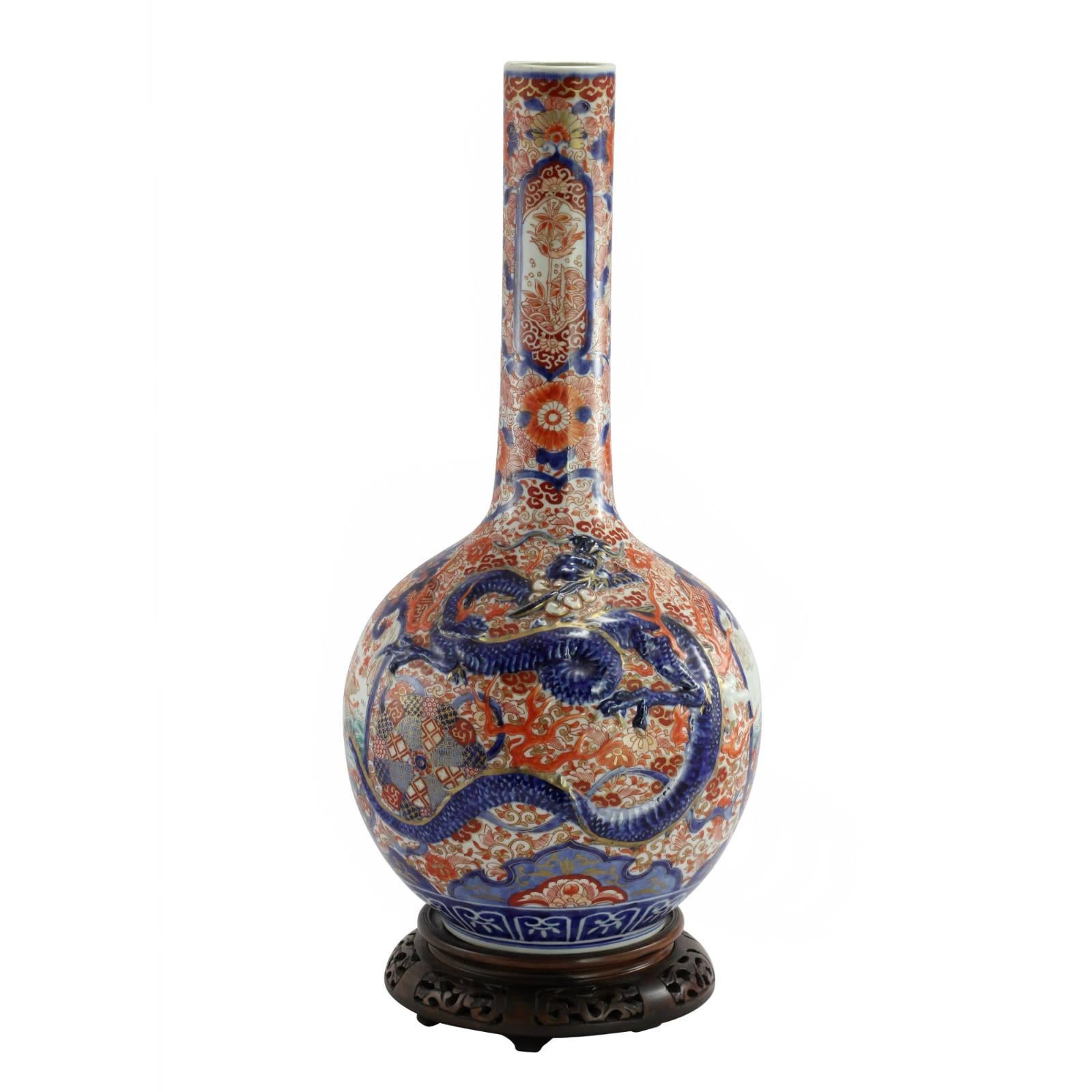 A Japanese Imari bottle vase, dating to the late Meiji era, decorated with a traditional cobalt blue, orange, and gilt gold color scheme. Two opposite sides of the vase feature hand painted panels of a man riding a giant fish (possibly a reference