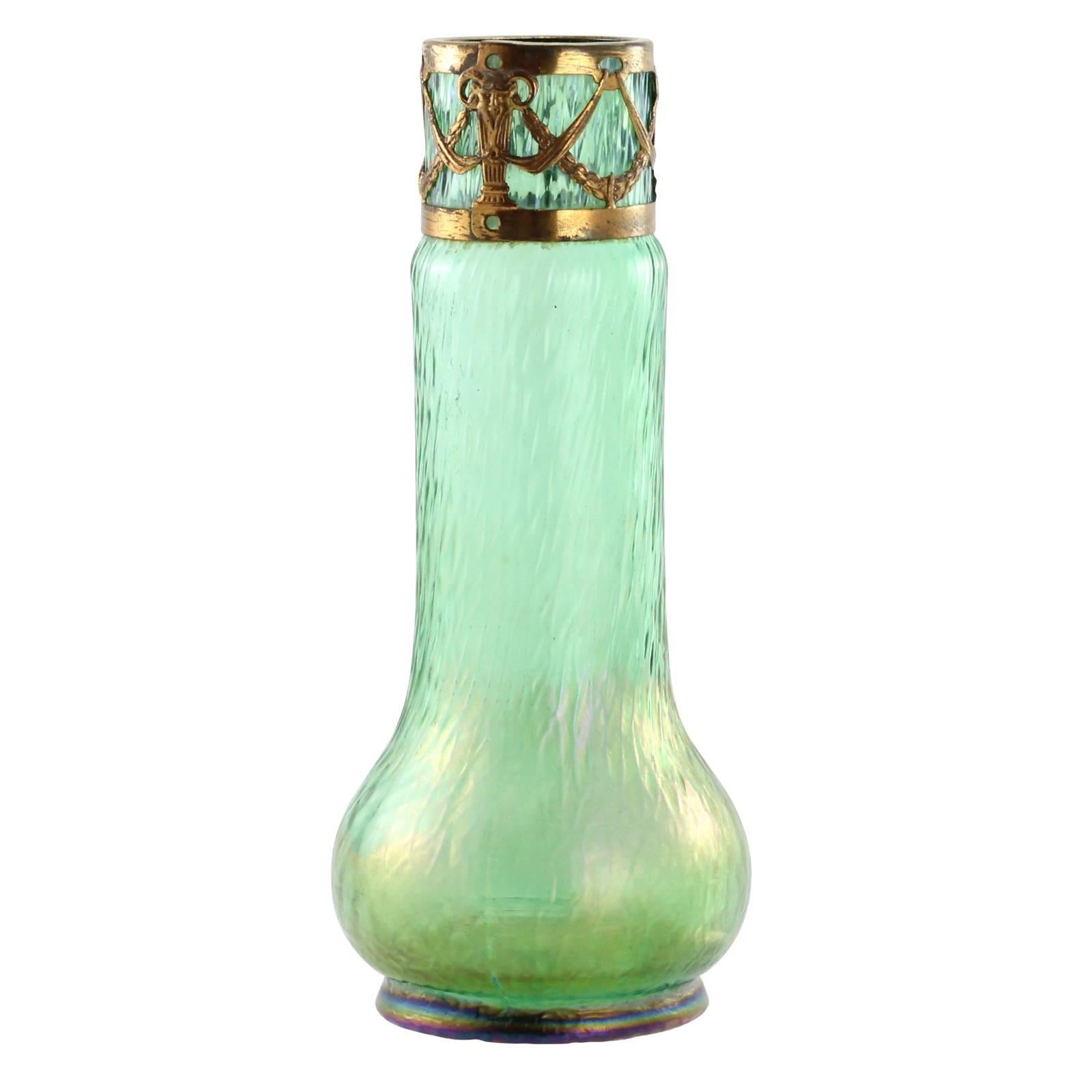 A late 19th century Art Nouveau glass vase by Carl Stölzle. Completed in a Martelé style decor (martele being French for 'hammered') on an iridescent green ground, the vase features a gilt metal collar decorated with swags and ram horned heads.
